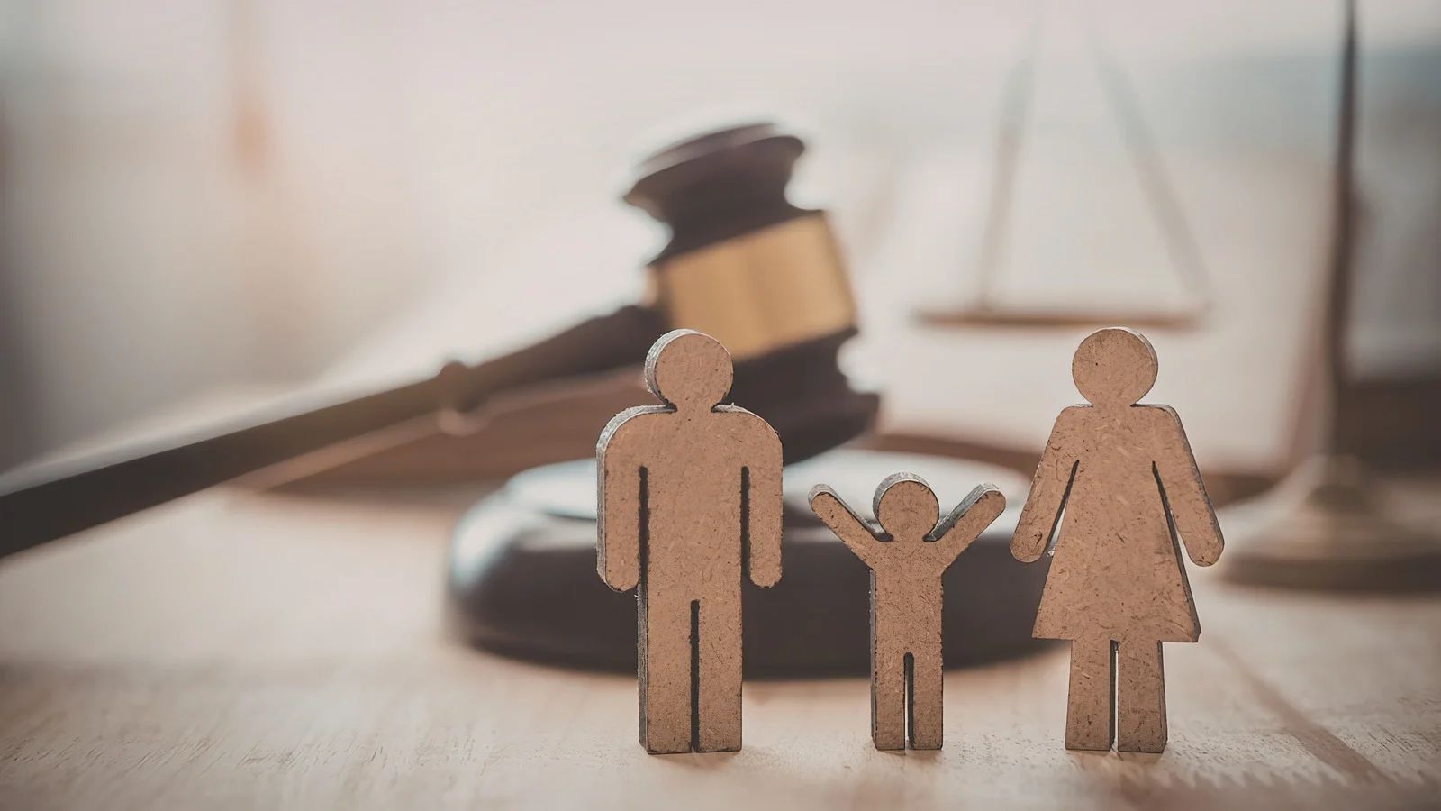 Cardboard cutouts of three figures standing in front of a wooden judge’s gavel and a blurry scale of justice.