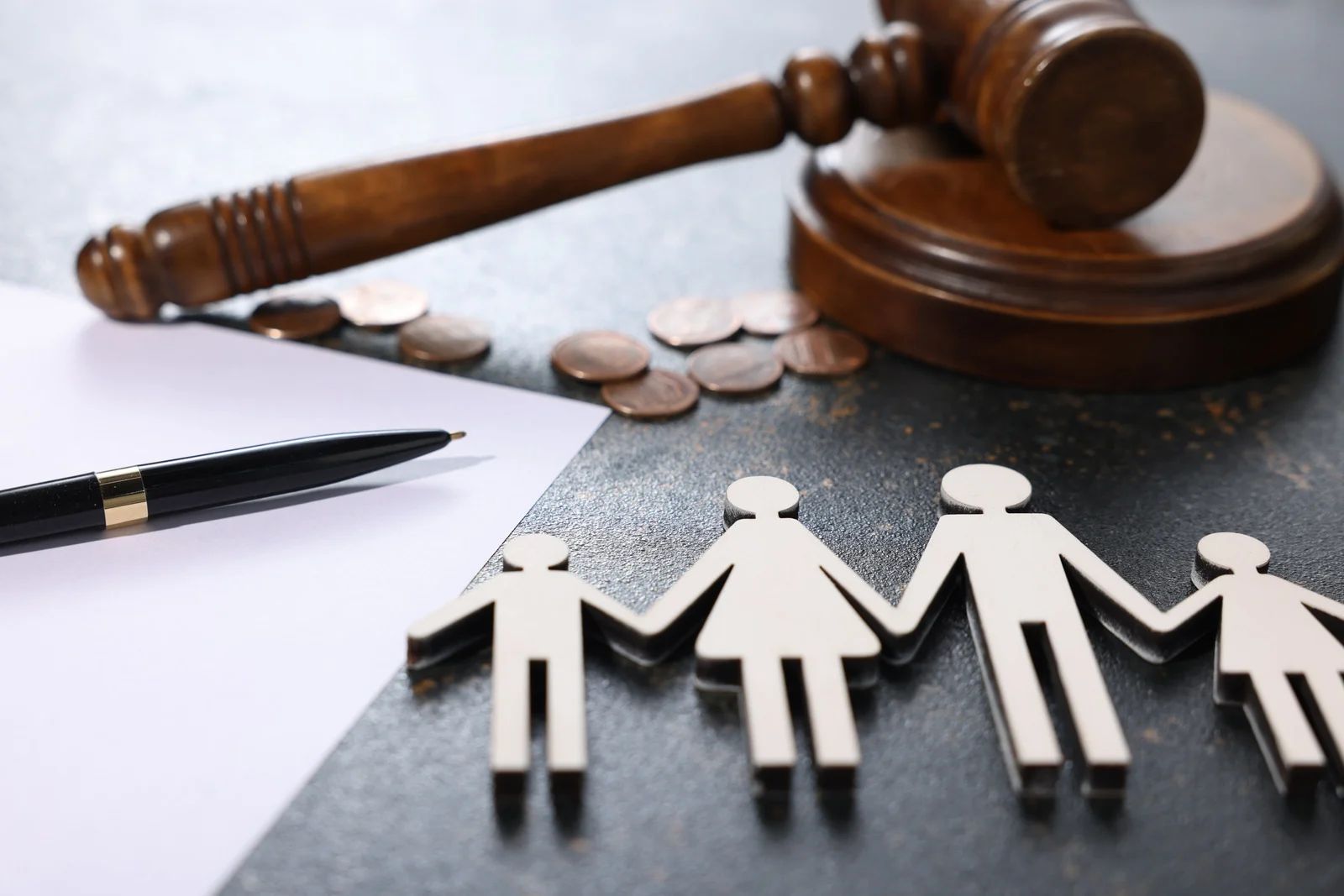 Paper family cutouts beside a gavel, pen, and coins on a table, suggesting family law or custody decisions
