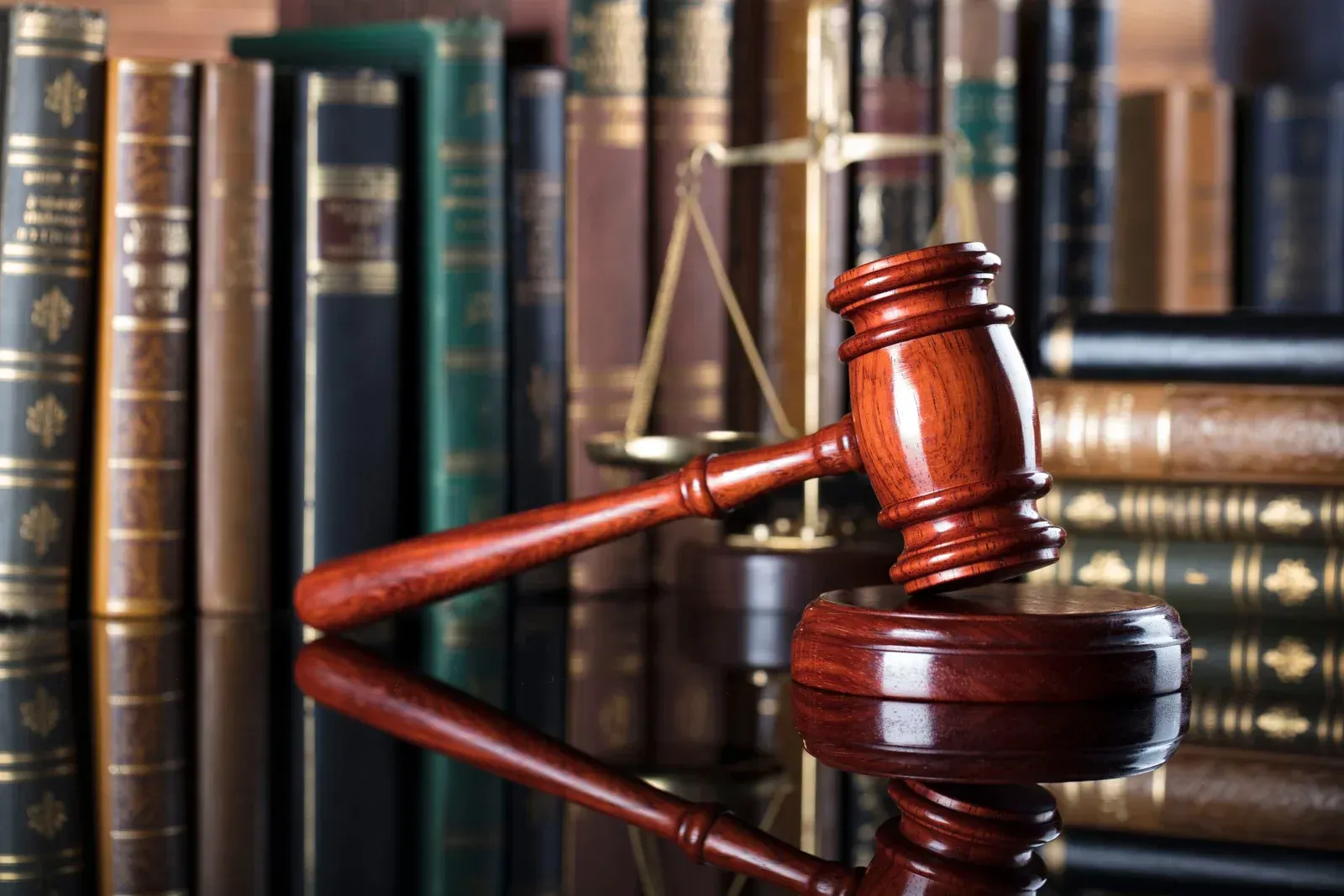 Judge’s gavel on a reflective desk in front of law books and scales of justice
