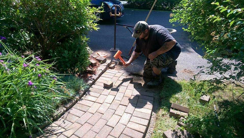 A man is working on a brick walkway in a garden.
