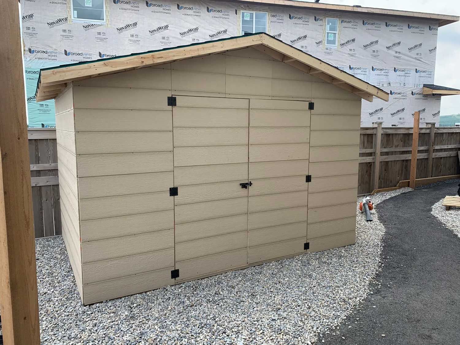 A small shed is sitting in front of a house under construction.