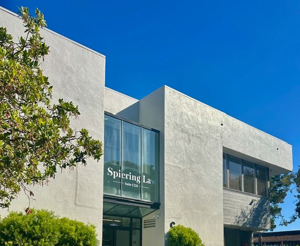 Modern white building with a glass entrance and a tree beside it under a blue sky