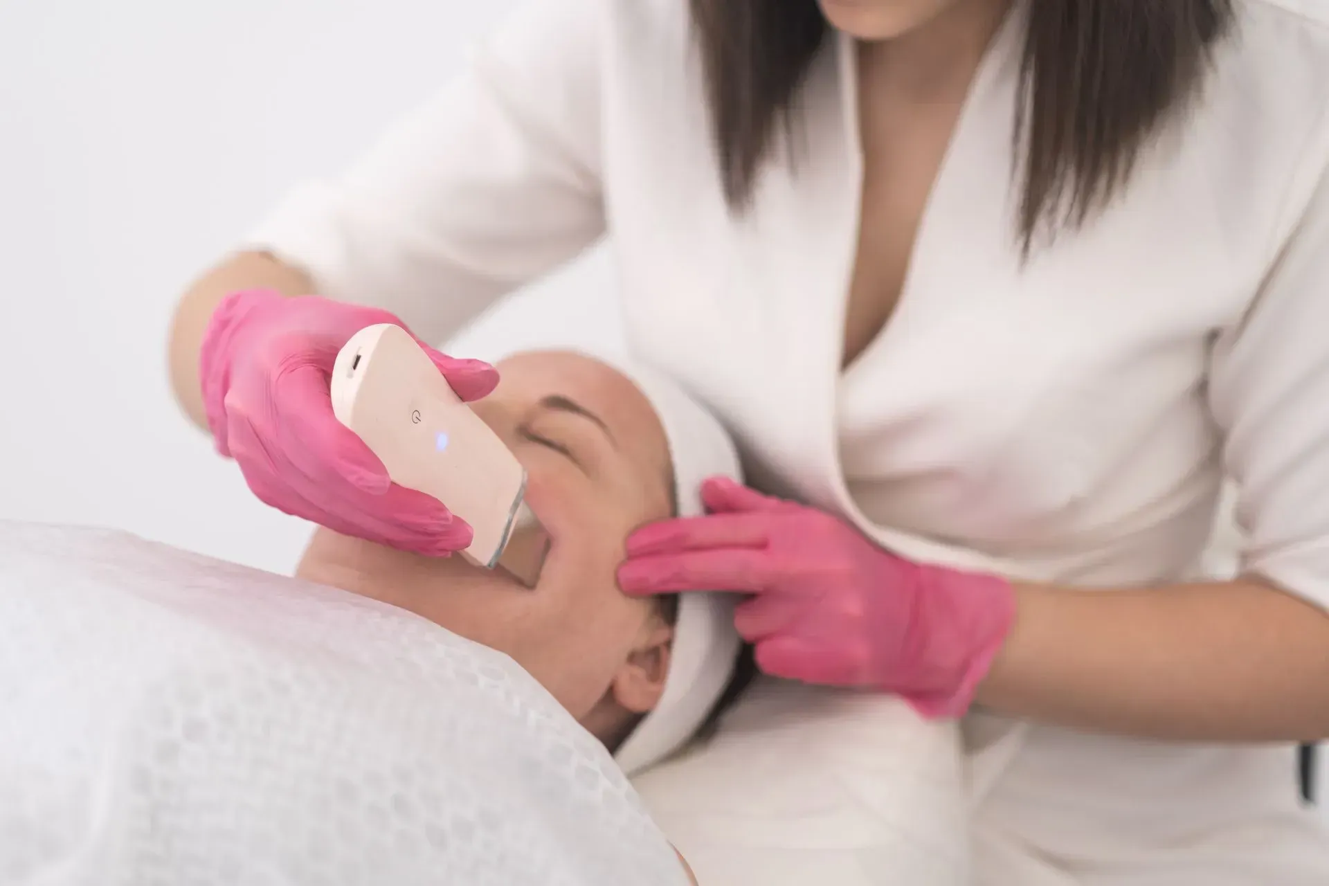 Esthetician using a handheld device on a client’s face during a skincare treatment