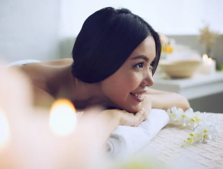 Woman resting on a bed, smiling in a bright room with soft white flowers nearby