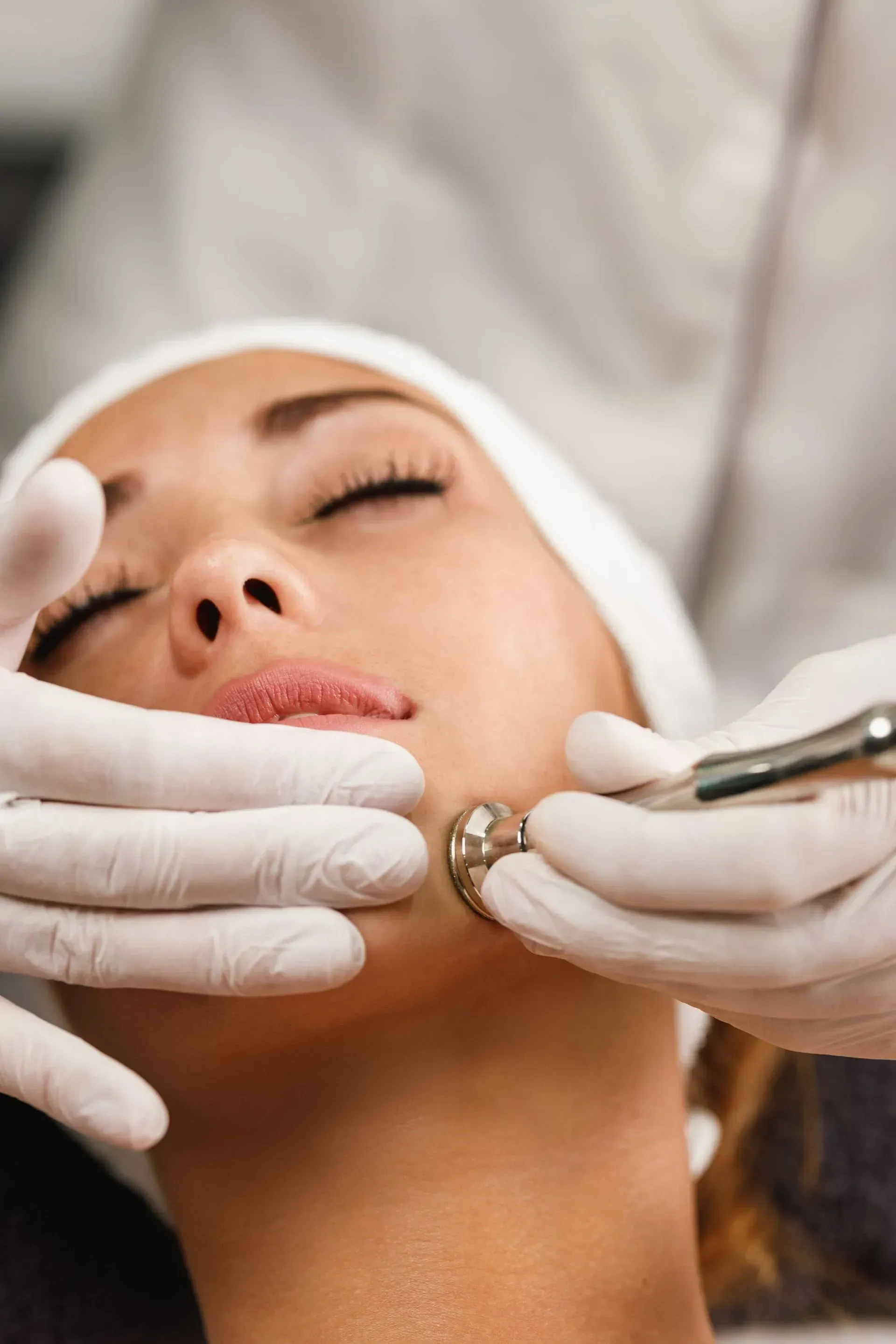 Cosmetic facial treatment with gloved hands using a metal tool on a woman’s chin