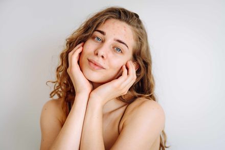 Woman with curly hair gently touching her face against a light background