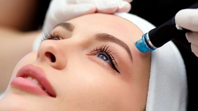 Esthetic treatment with gloved hands using a blue facial device on a woman’s forehead