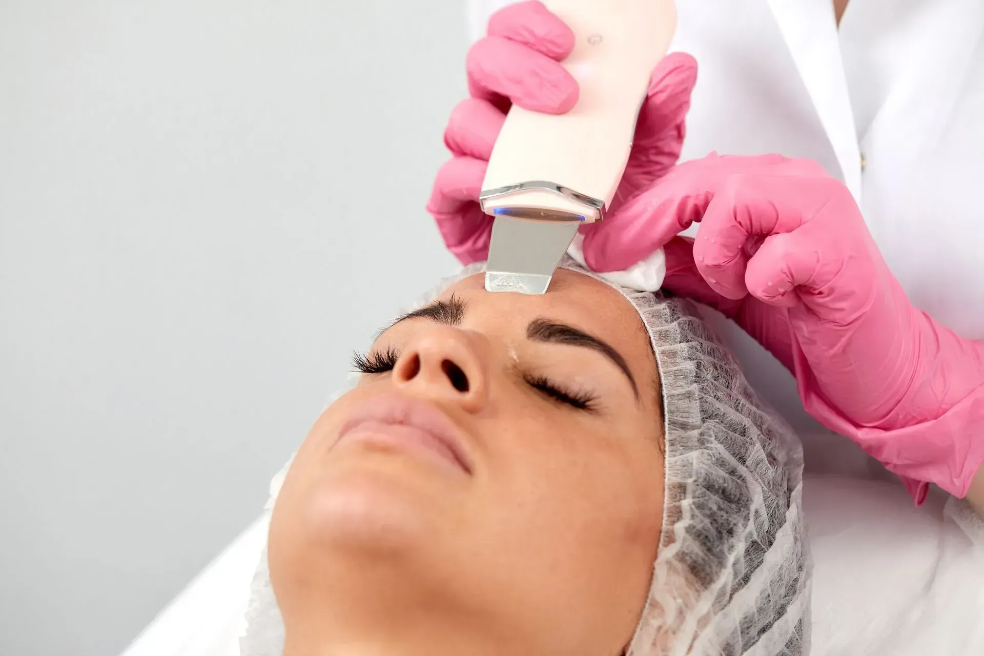 Gloved hands using a handheld device on a woman's forehead during a facial treatment