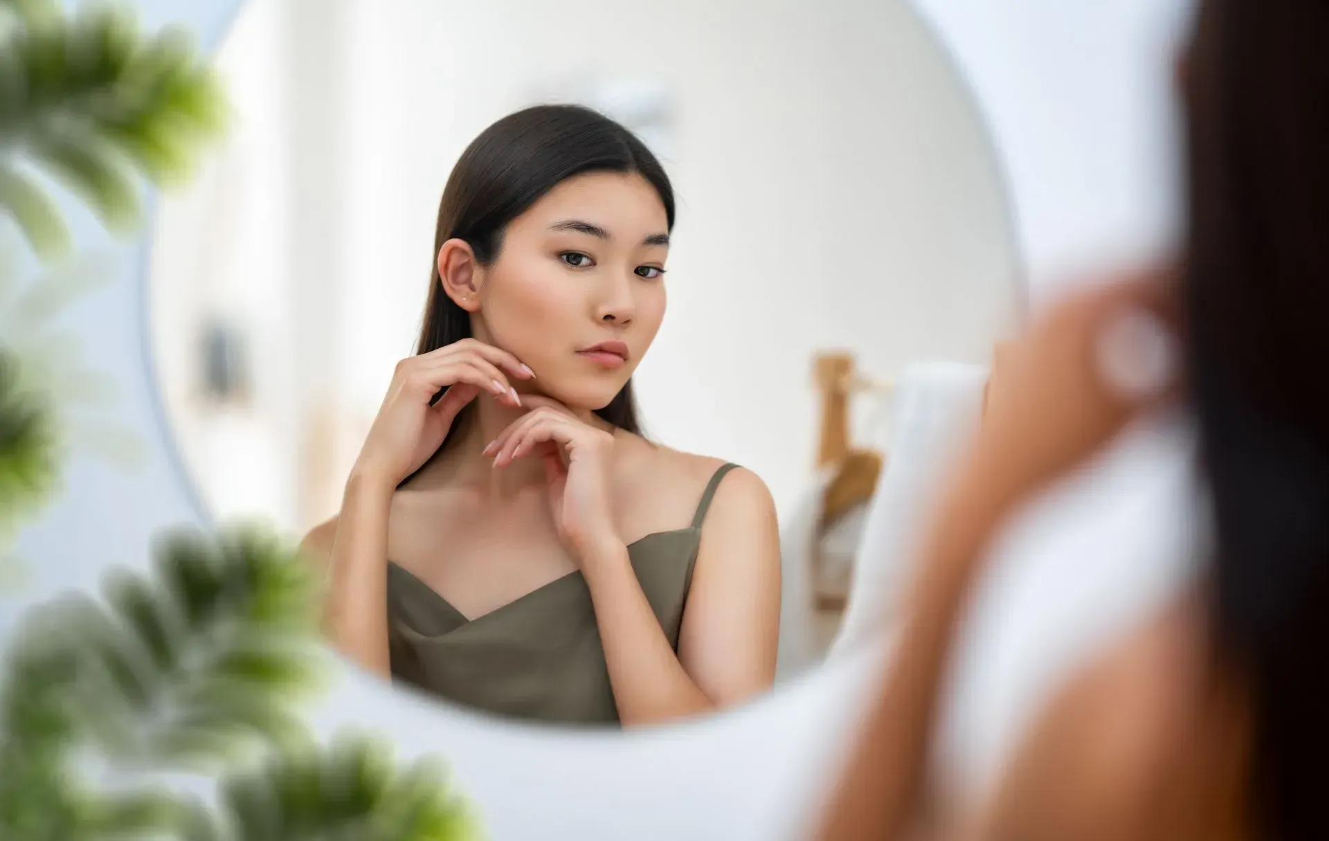 Woman looking into a mirror while adjusting her pose, with a blurred foreground and soft indoor lighting