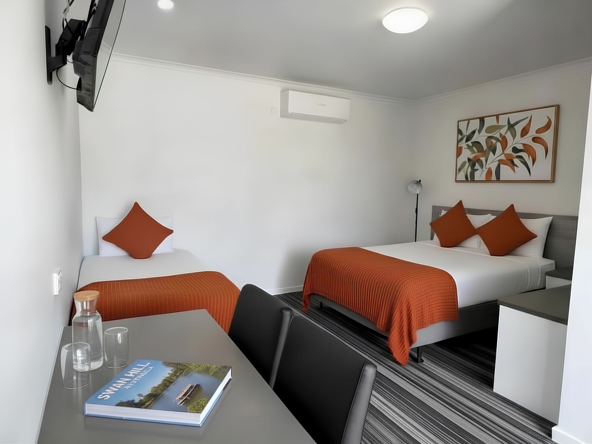 Hotel room with a queen bed and a single bed. A table with chairs and a TV on the wall.