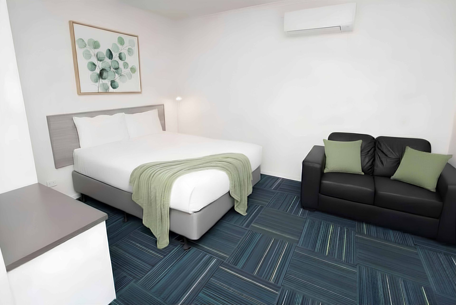 Bedroom with a bed, small sofa, blue patterned carpet, and wall-mounted air conditioner.