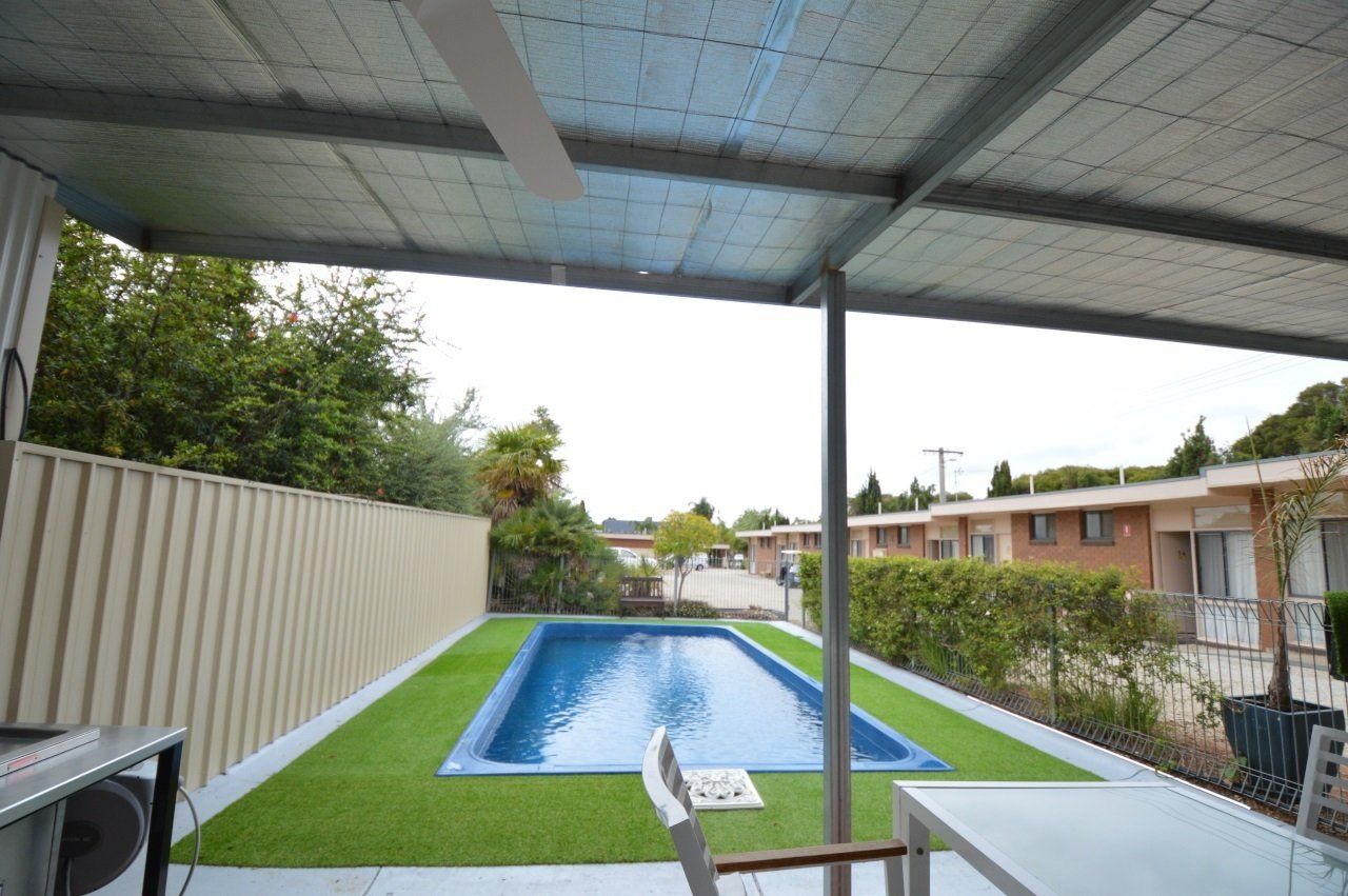 Backyard patio with a small pool, artificial turf, and a view of neighboring buildings.