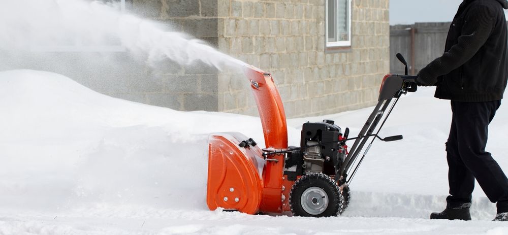 A man is pushing a snow blower in the snow.