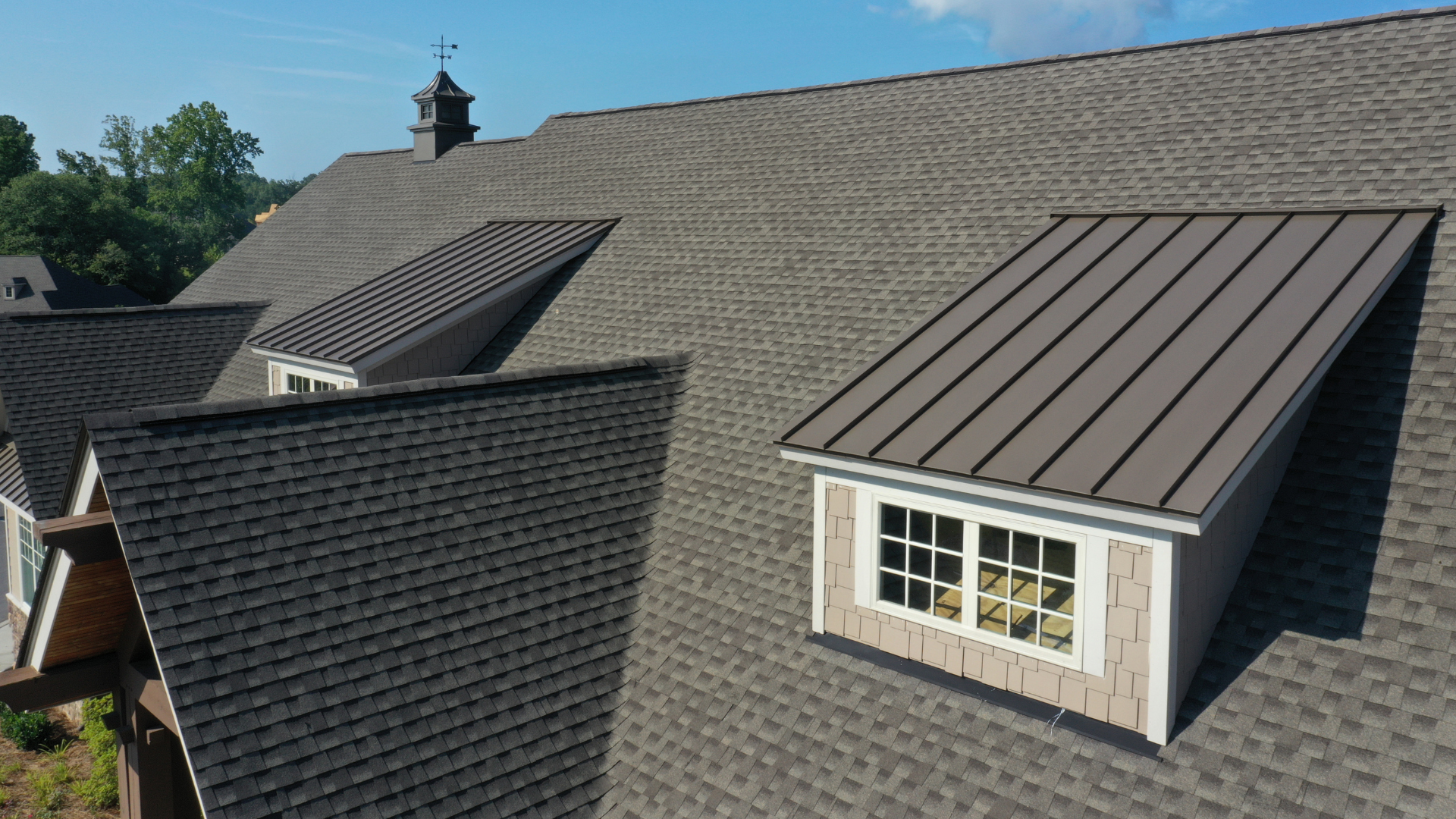 Roof with dark shingles and two dormer windows under a blue sky