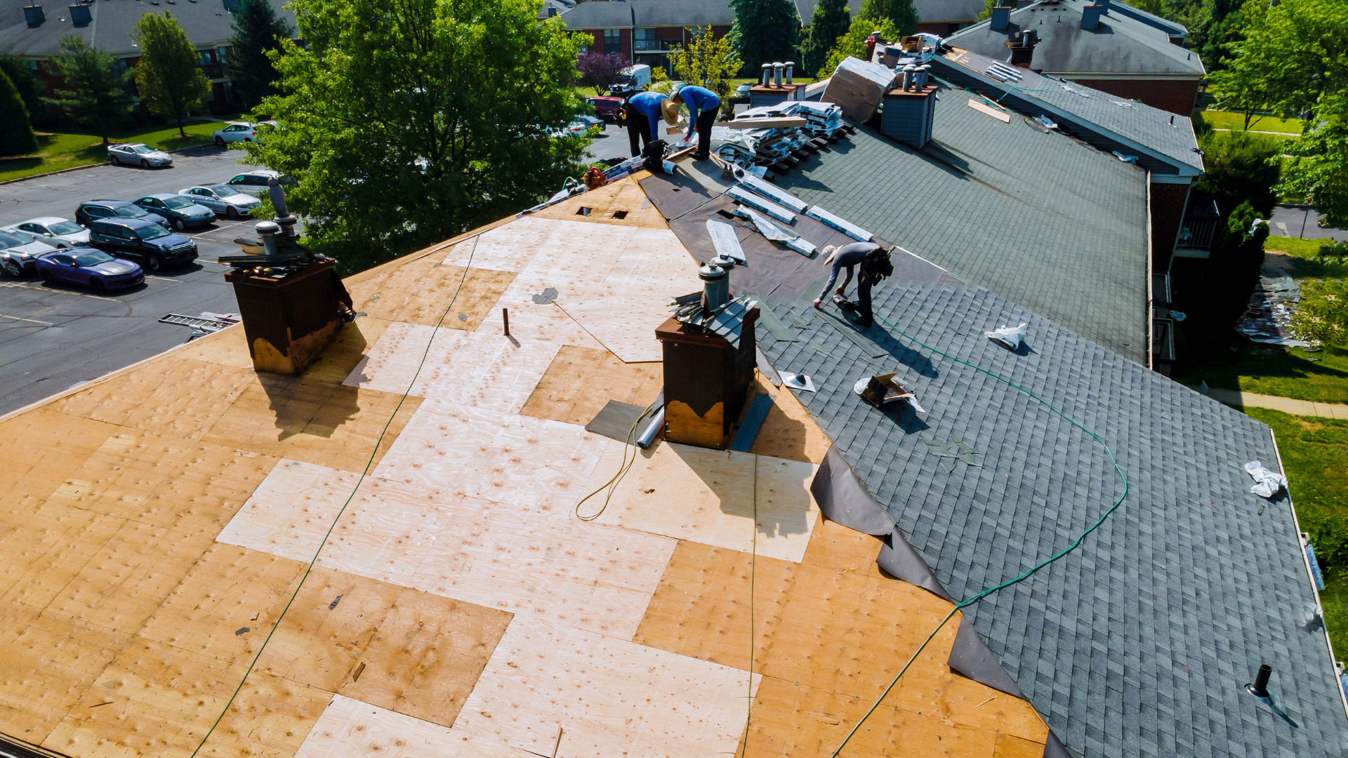 Roofers installing shingles on a house roof, with orange underlayment and gray roofing sections visible.