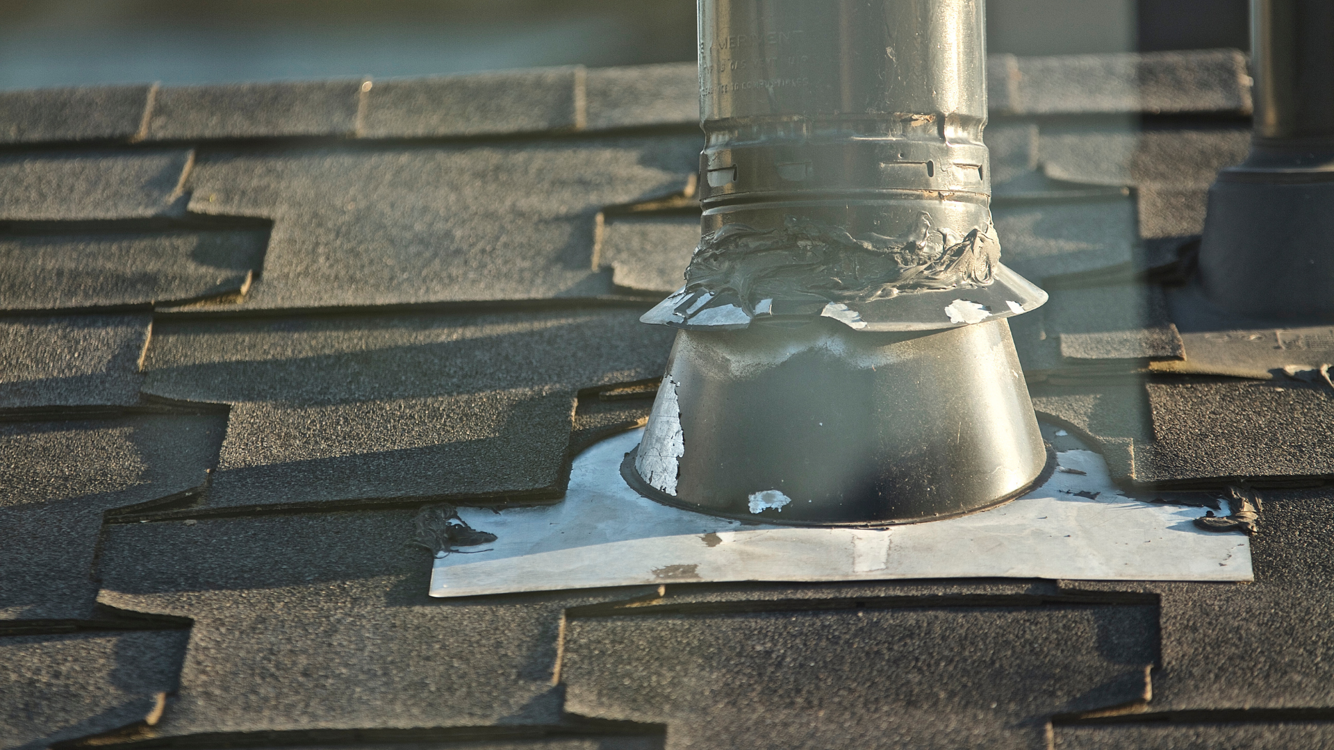 Roof vent pipe with metal flashing and sealant on dark asphalt shingles