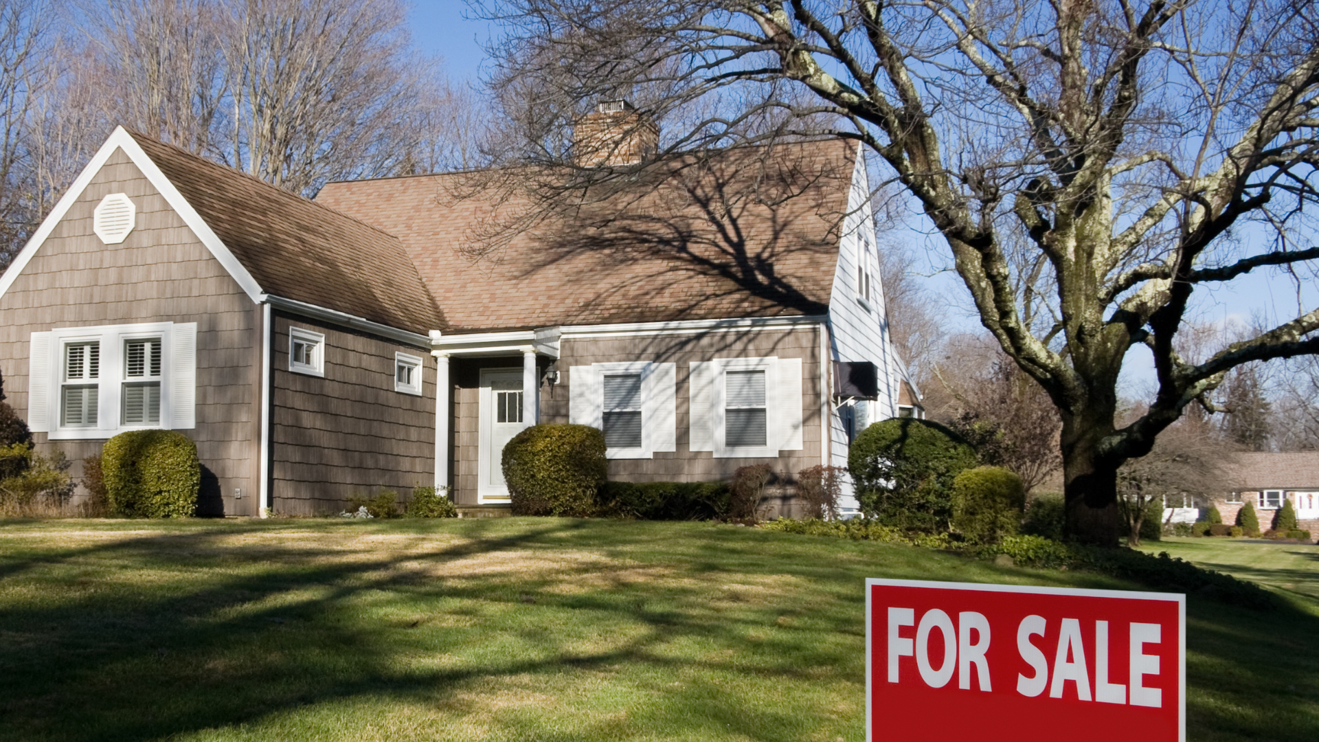 Suburban house with a red “For Sale” sign in the front yard