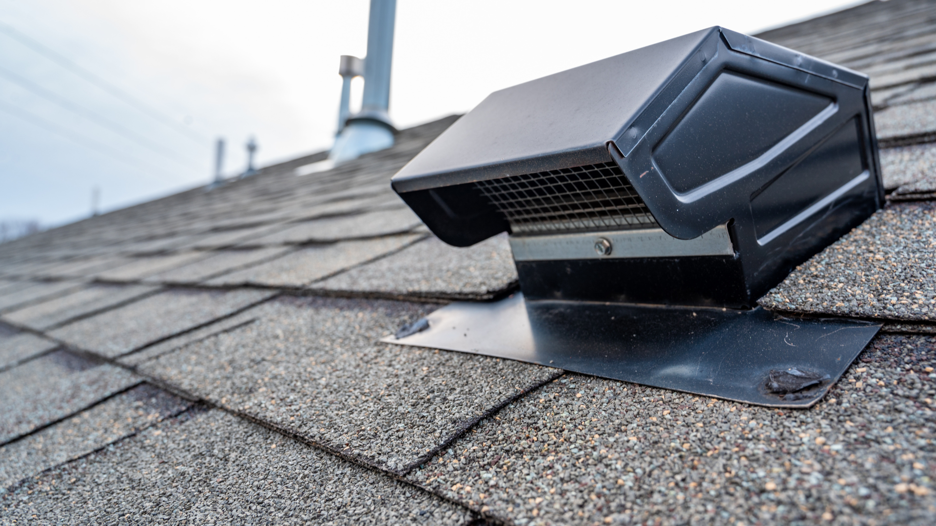 Roof-mounted ventilation fan on gray shingle shingles with a black vent hood and flashing