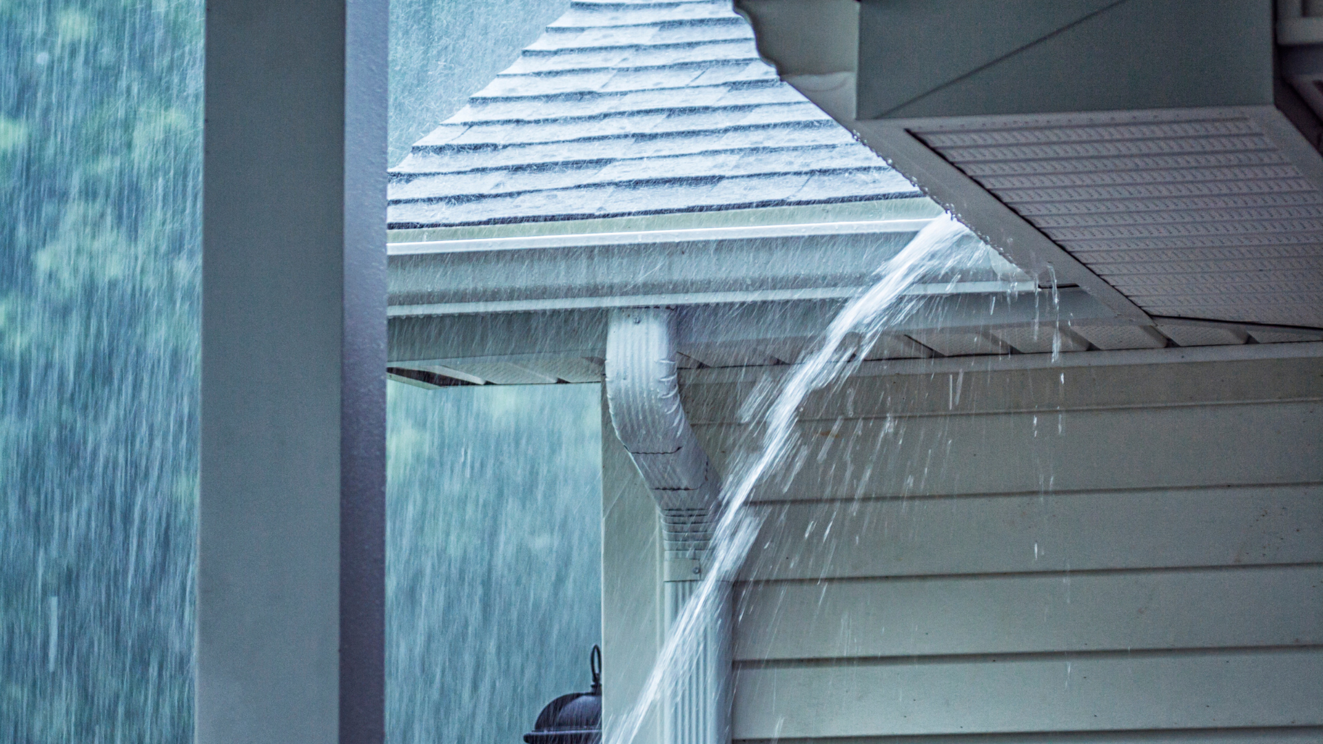 Rain pouring from a roof gutter onto a house exterior during a storm
