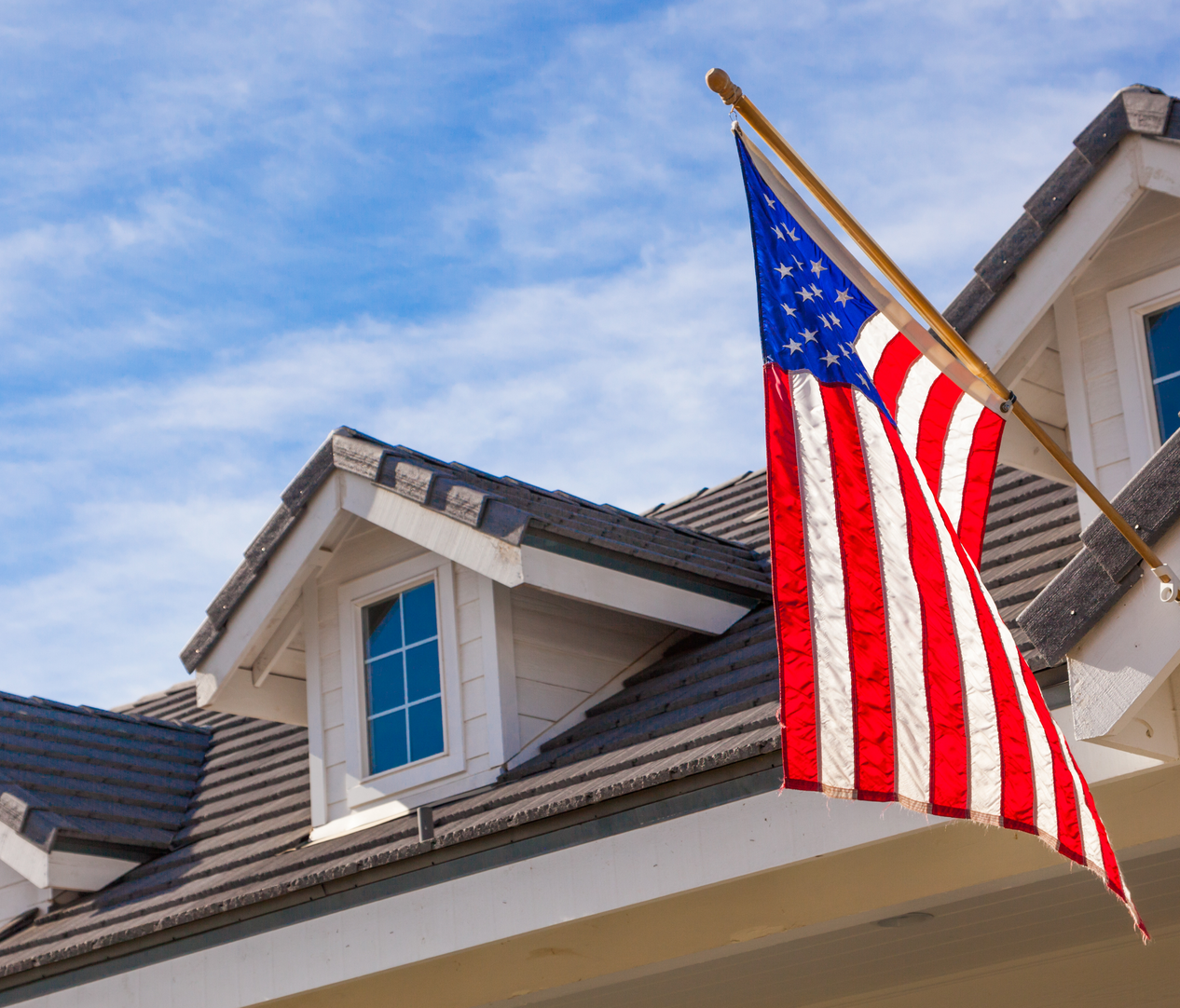American flag hanging from a suburban house roof against a blue sky