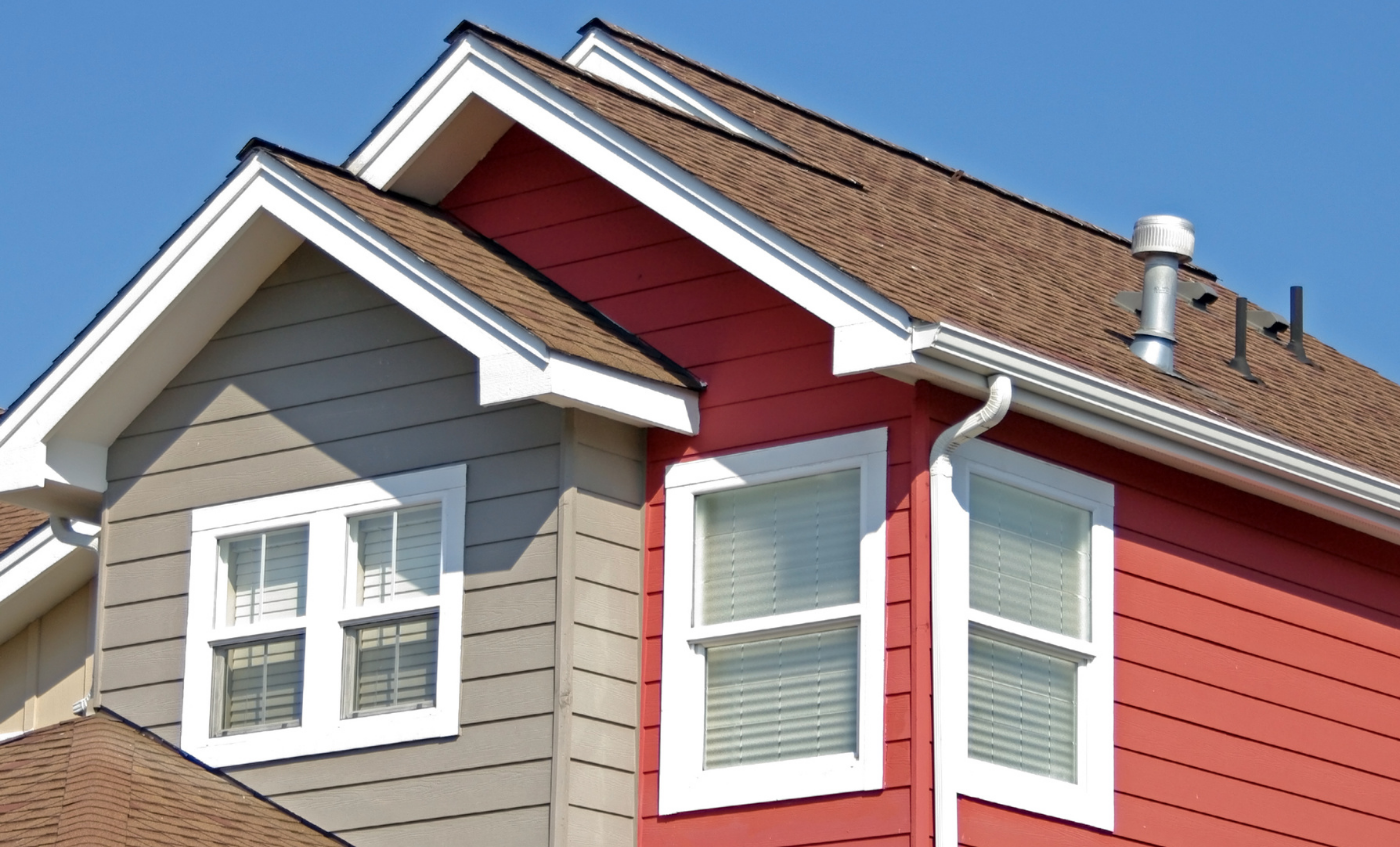 Red and gray house exterior with white-trimmed windows and a sloped shingle roof