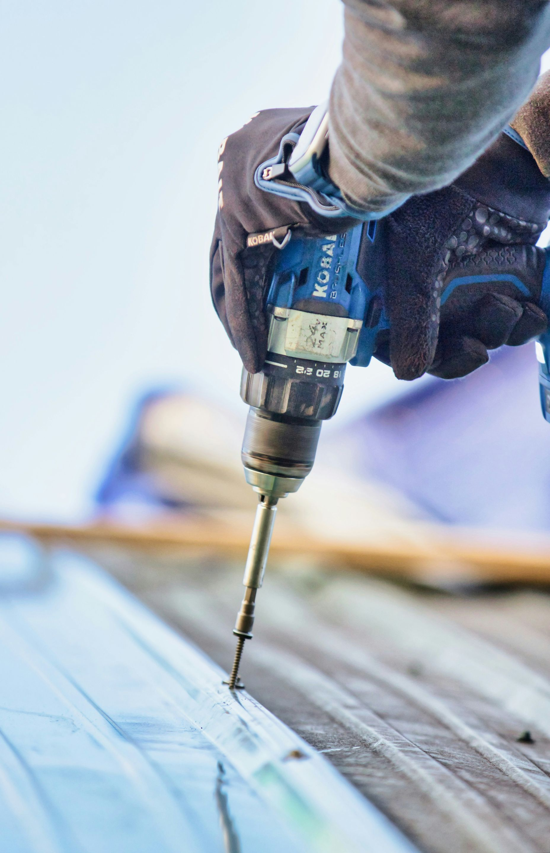 Gloved hand using a power drill on a wooden plank outdoors
