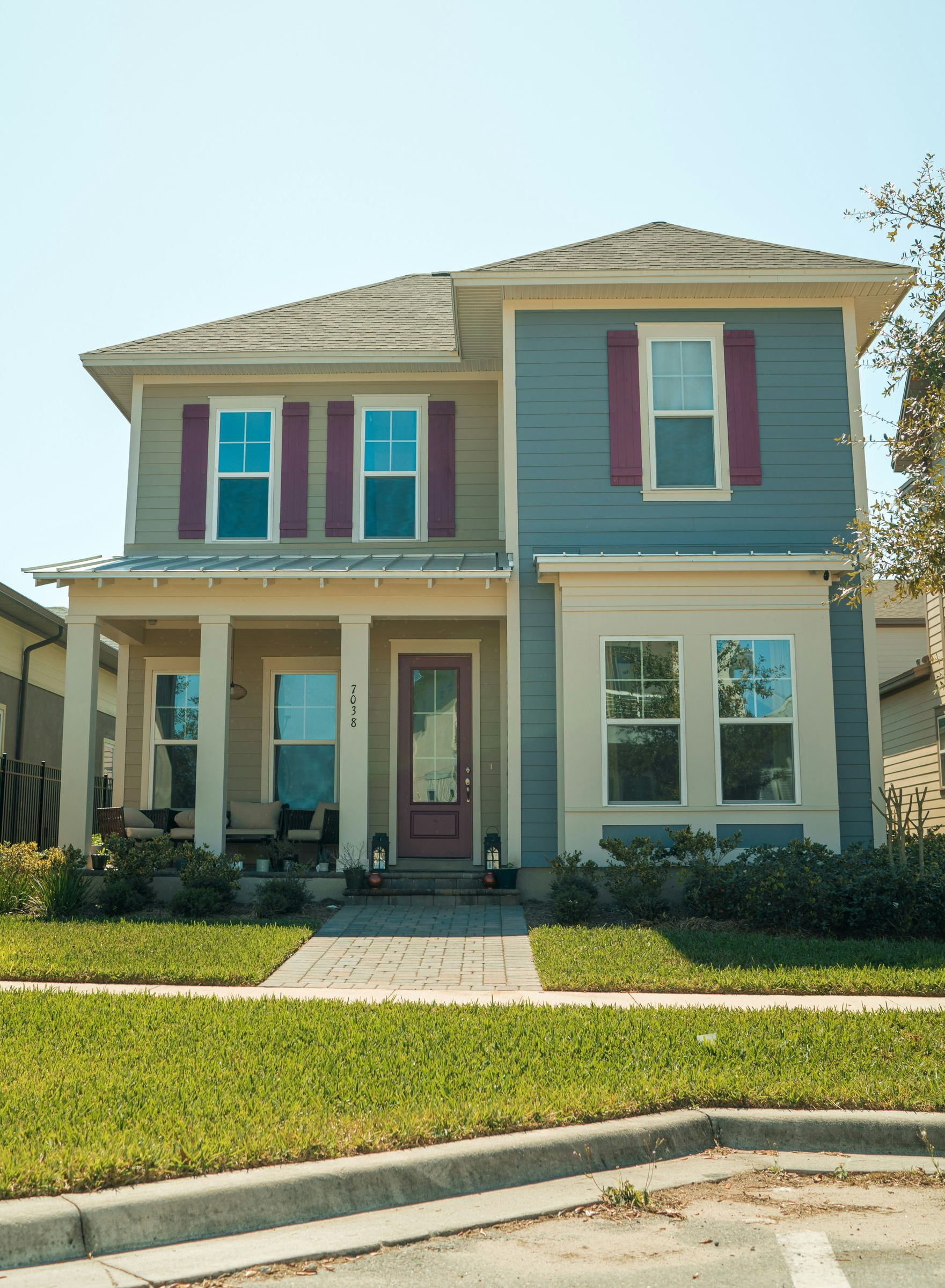 Two-story beige and blue house with a front porch, pink shutters, and a green lawn