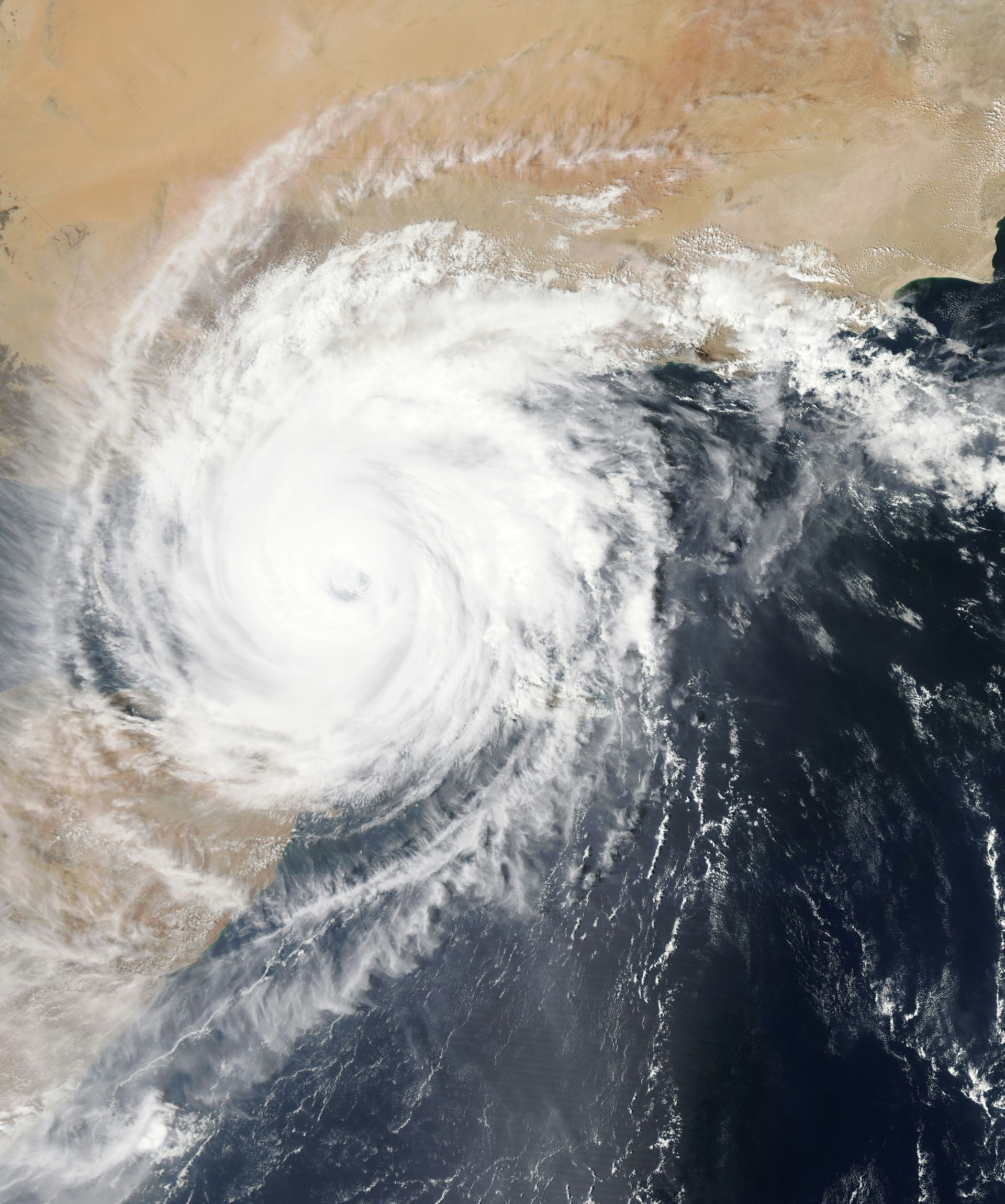 Satellite view of a swirling white cyclone over dark ocean and tan land