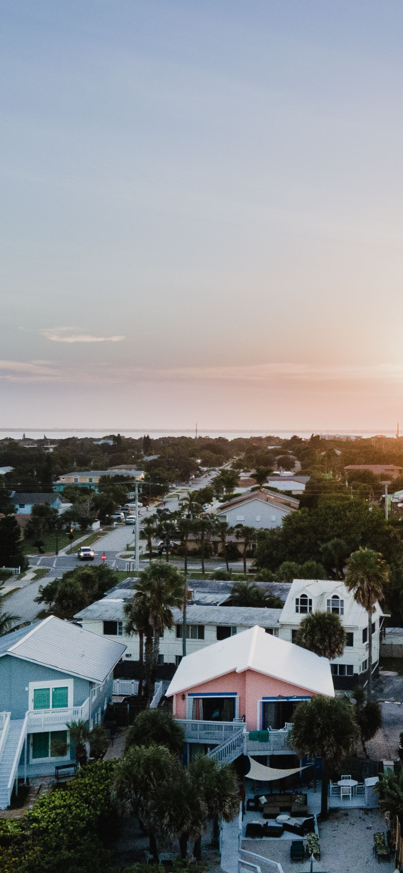 Pastel sunset over a coastal neighborhood with palm trees and houses