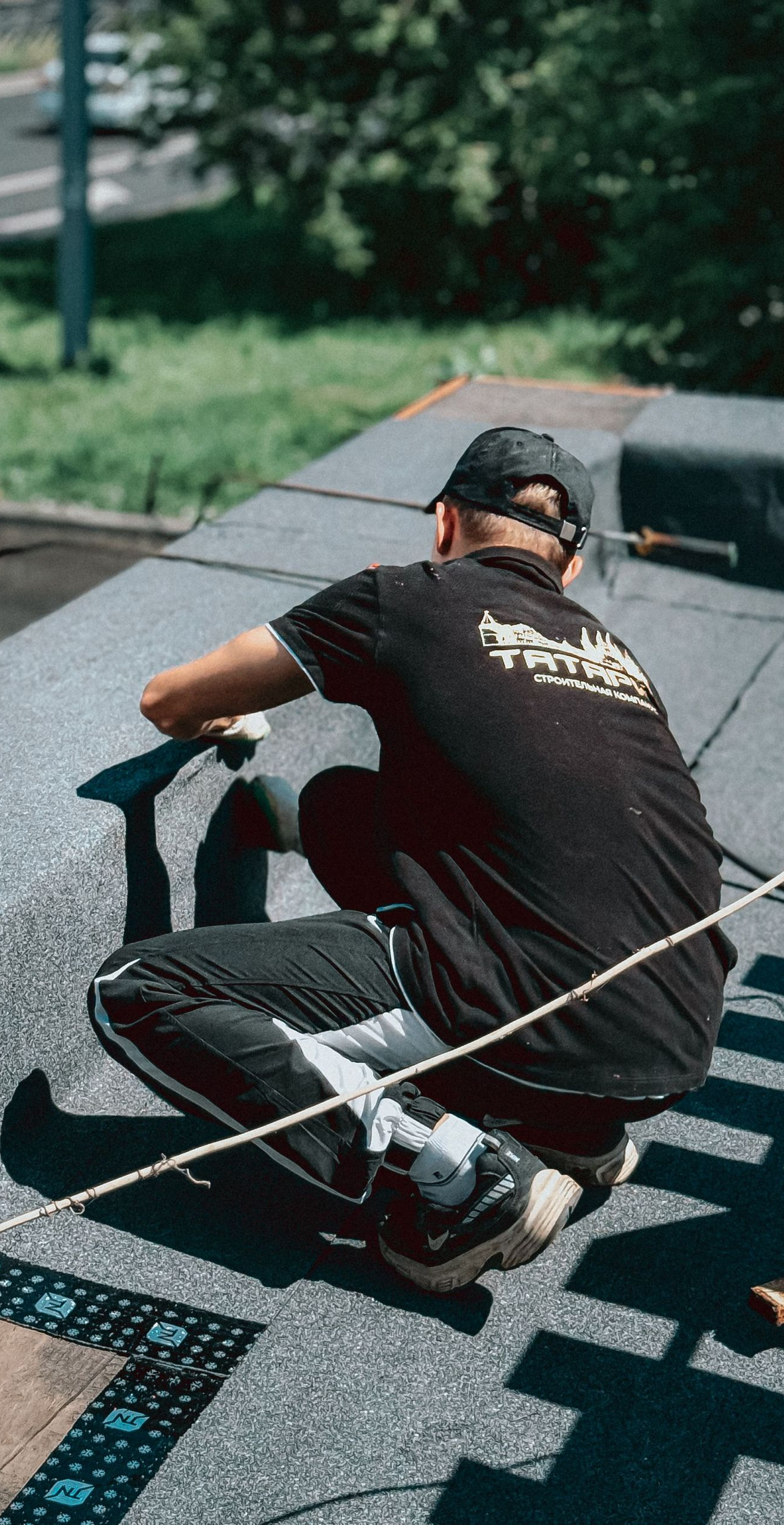 Person crouching on a rooftop, working near a blue tarp and safety rope.