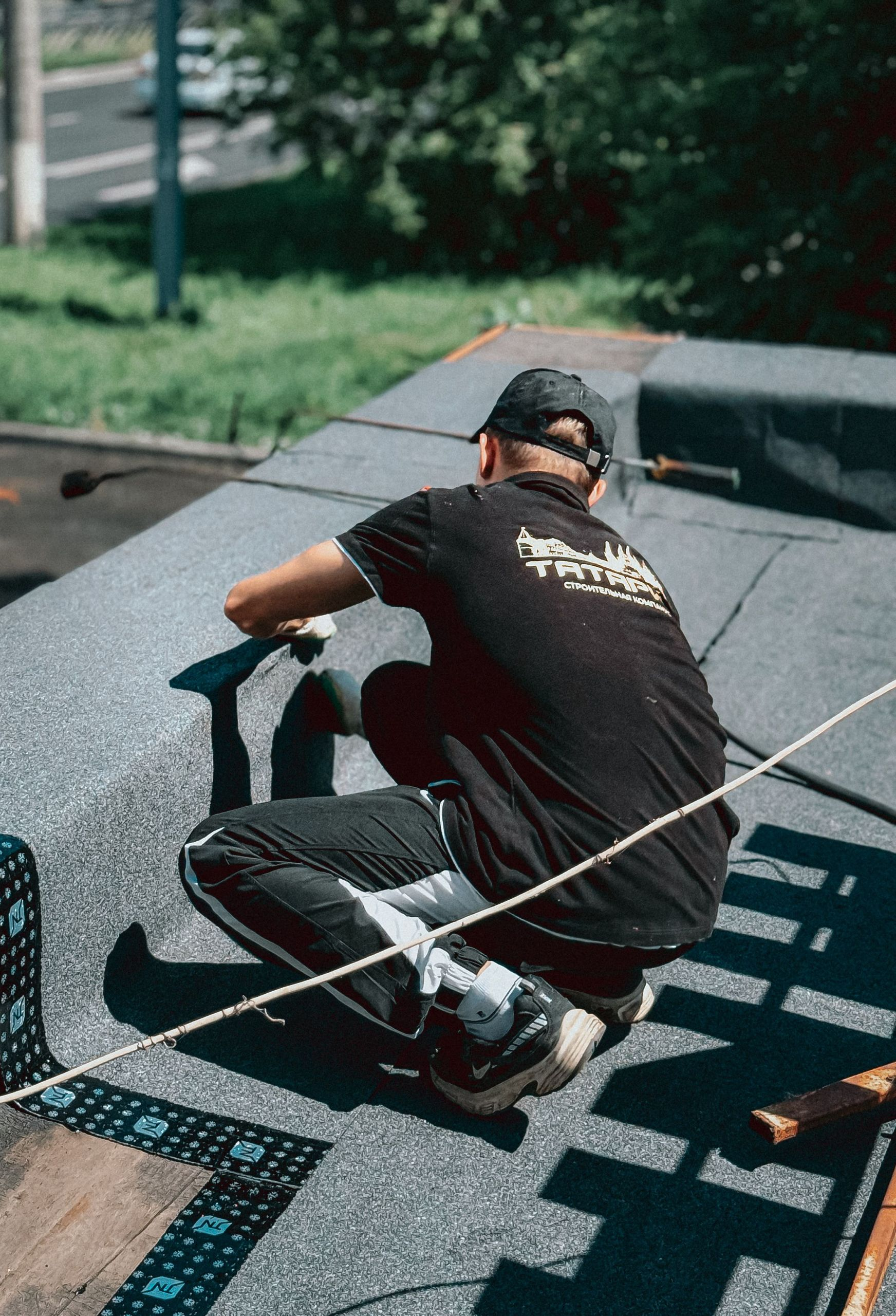 Person crouching on a rooftop, working near a blue tarp and safety rope.