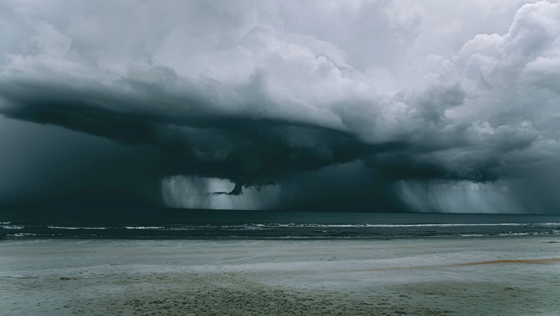 Dark storm clouds over a beach with heavy rain in the distance