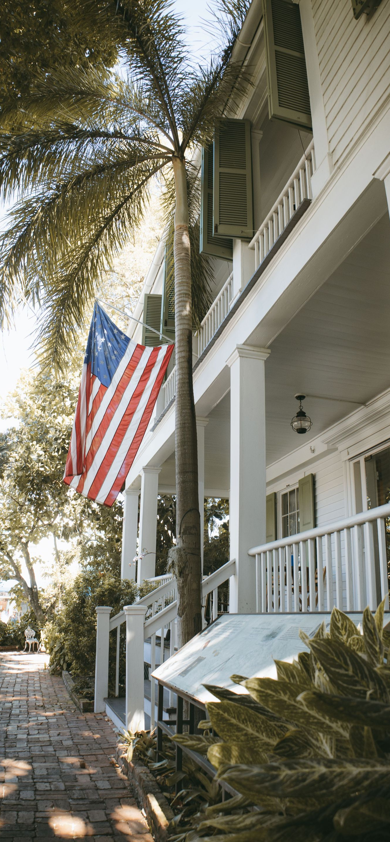 White house porch with an American flag beside a tree-lined walkway