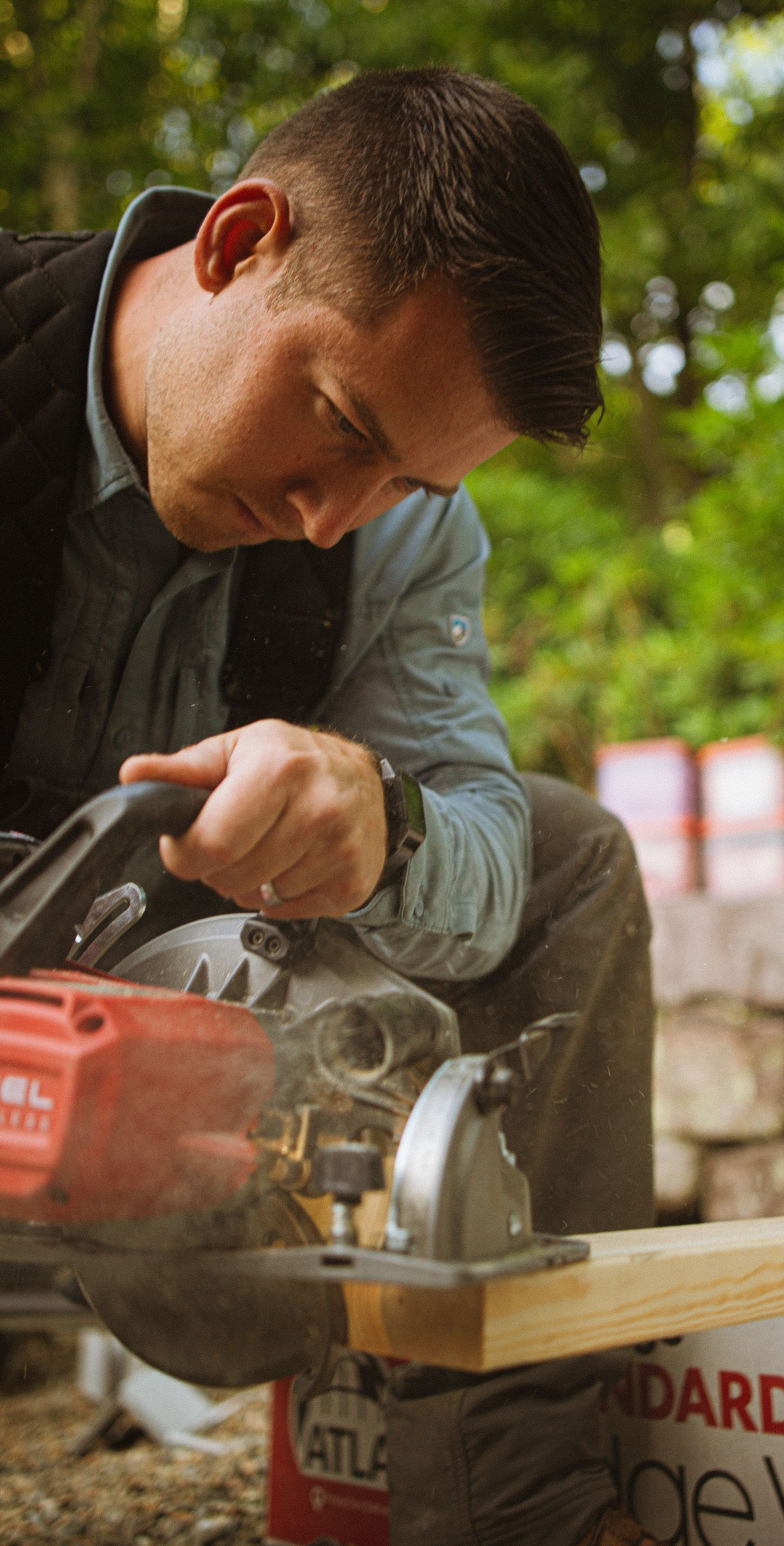 Worker cutting metal with a power saw, wearing a dark vest and focusing on the task outdoors.