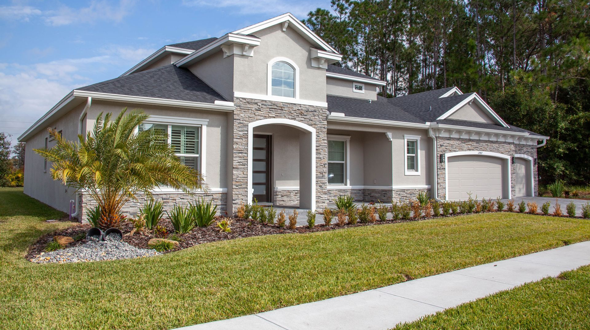 Suburban single-story gray house with white trim, front lawn, and driveway under a blue sky