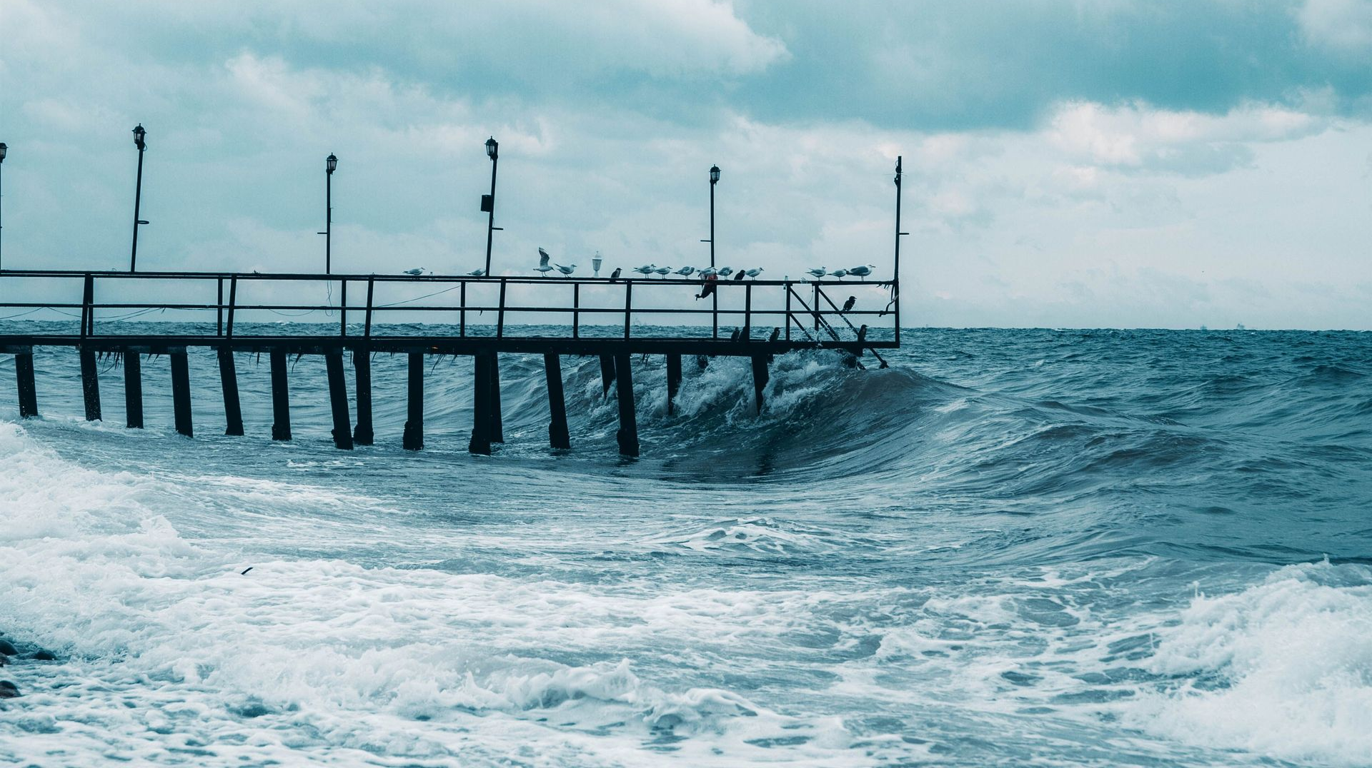 Stormy sea beside a pier with waves crashing under a cloudy sky