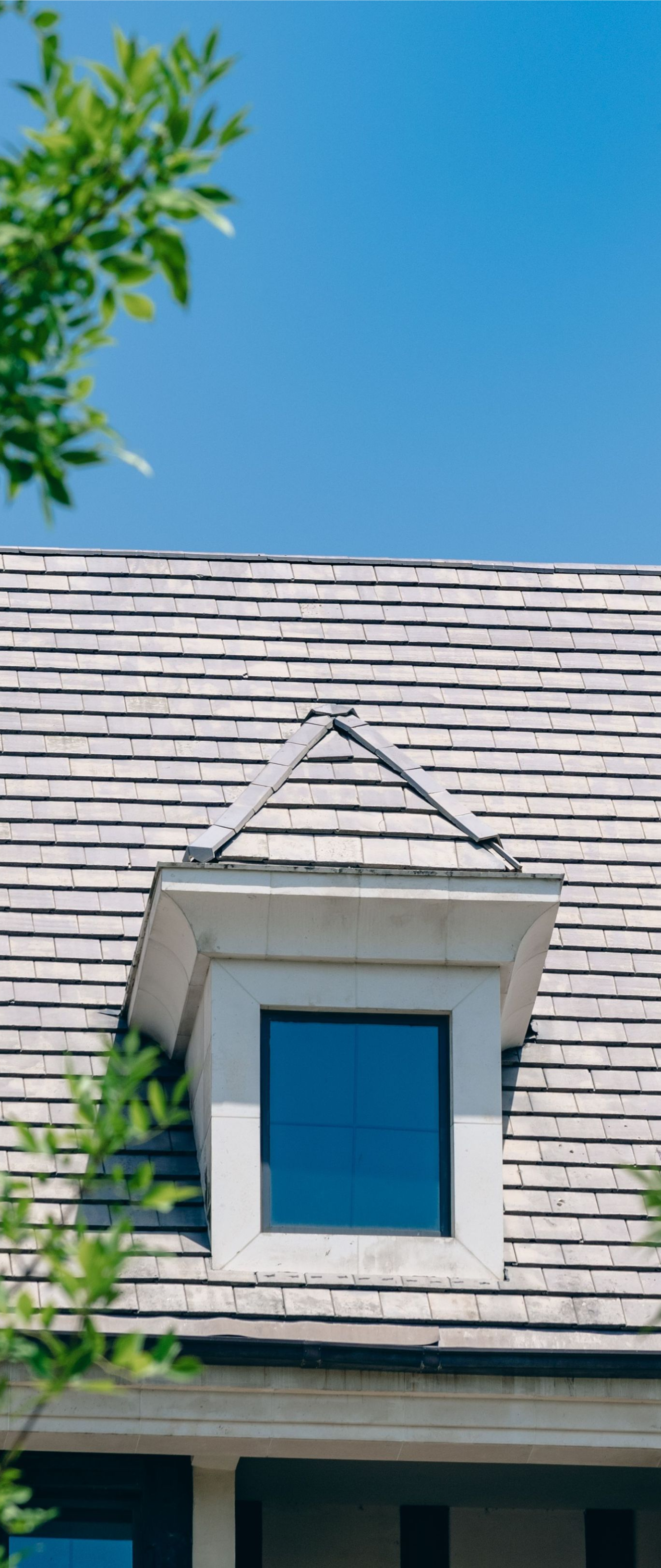 Blue dormer window on a shingled roof against a clear blue sky