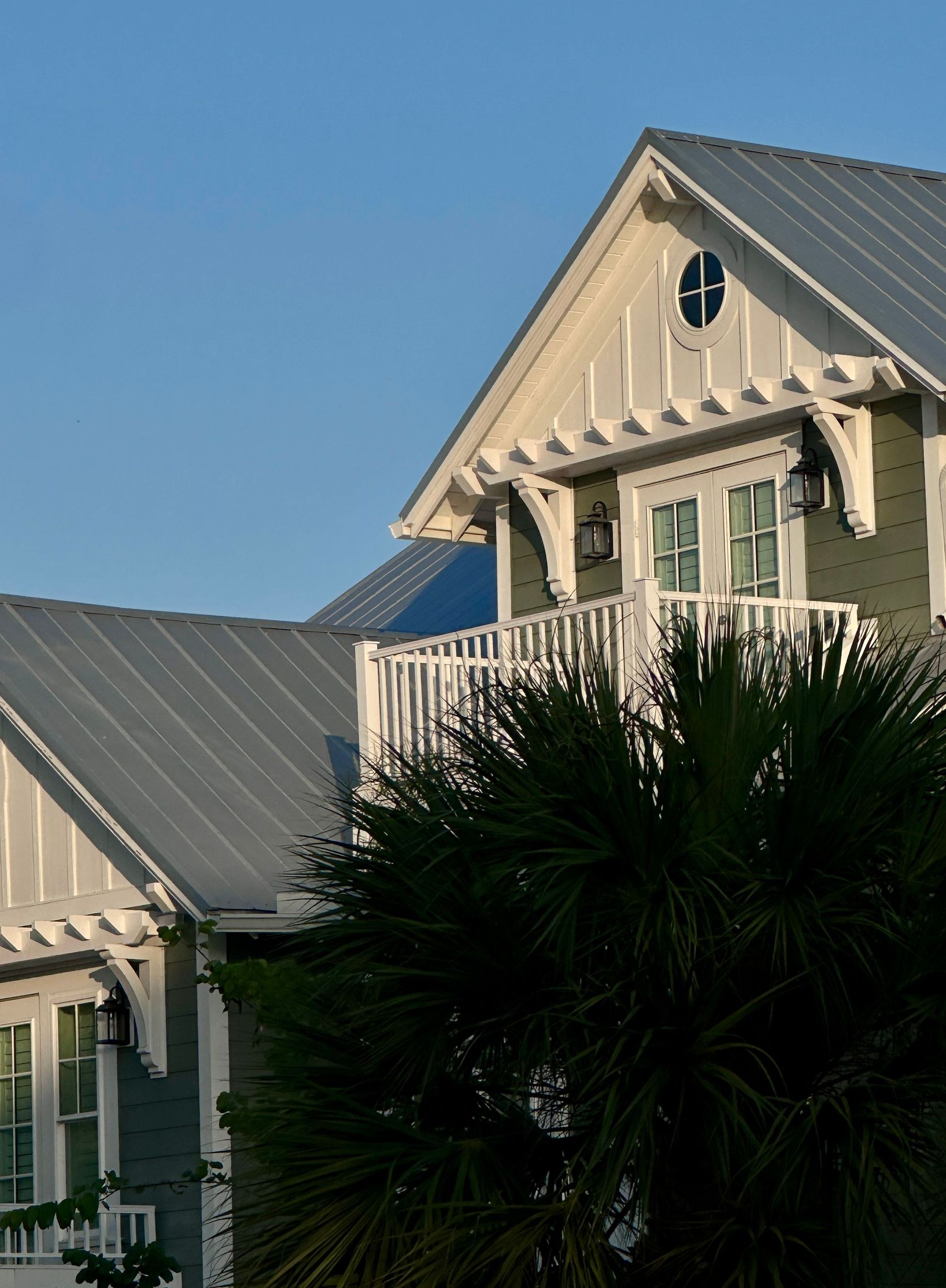White house with gray roof and green shutters behind palm trees under a clear blue sky