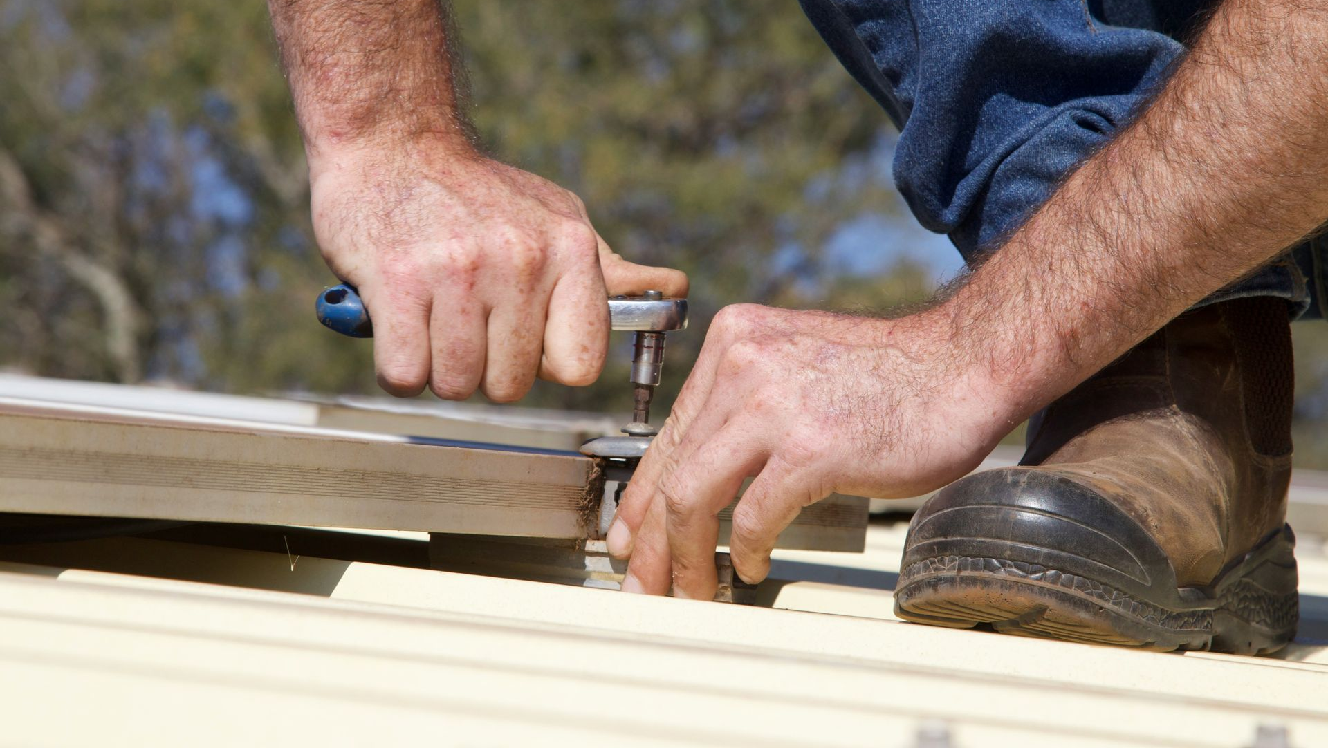 Hands using a hammer to install roofing panels on a roof outdoors