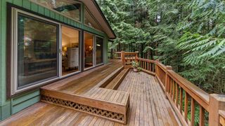 A large wooden deck with stairs leading up to it is in front of a house surrounded by trees.