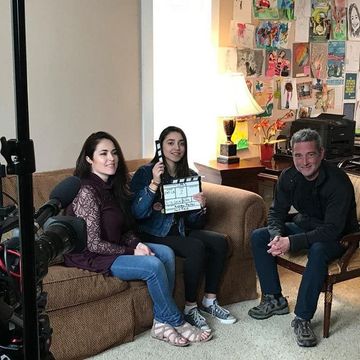 Three people are sitting on a couch holding a clapper board.