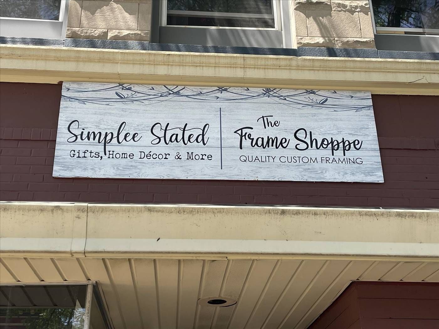 Two white signs on a building facade reading “Simple Stated” and “The Frame Shoppe”
