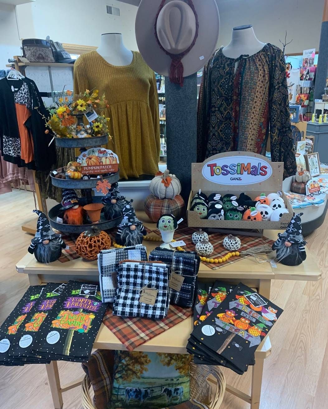 Display table with Halloween decorations, candy, pumpkin-themed items, and patterned sweaters in a shop.