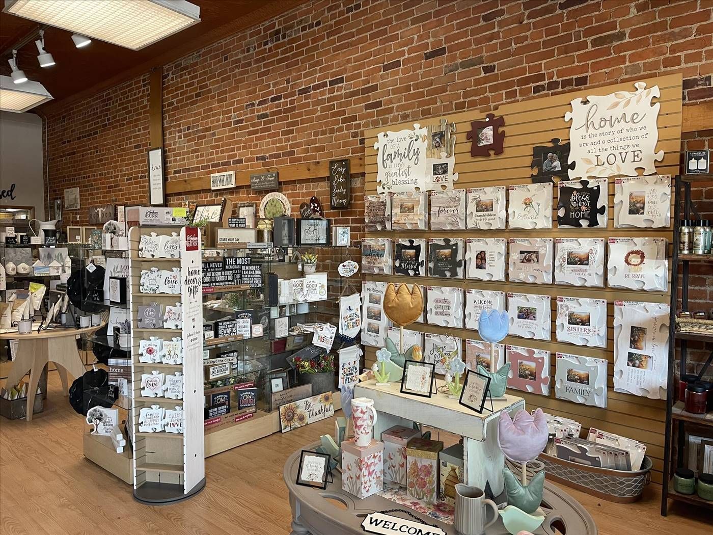 Gift shop interior with wooden shelves of cards, framed art, and small home decor items under brick walls.