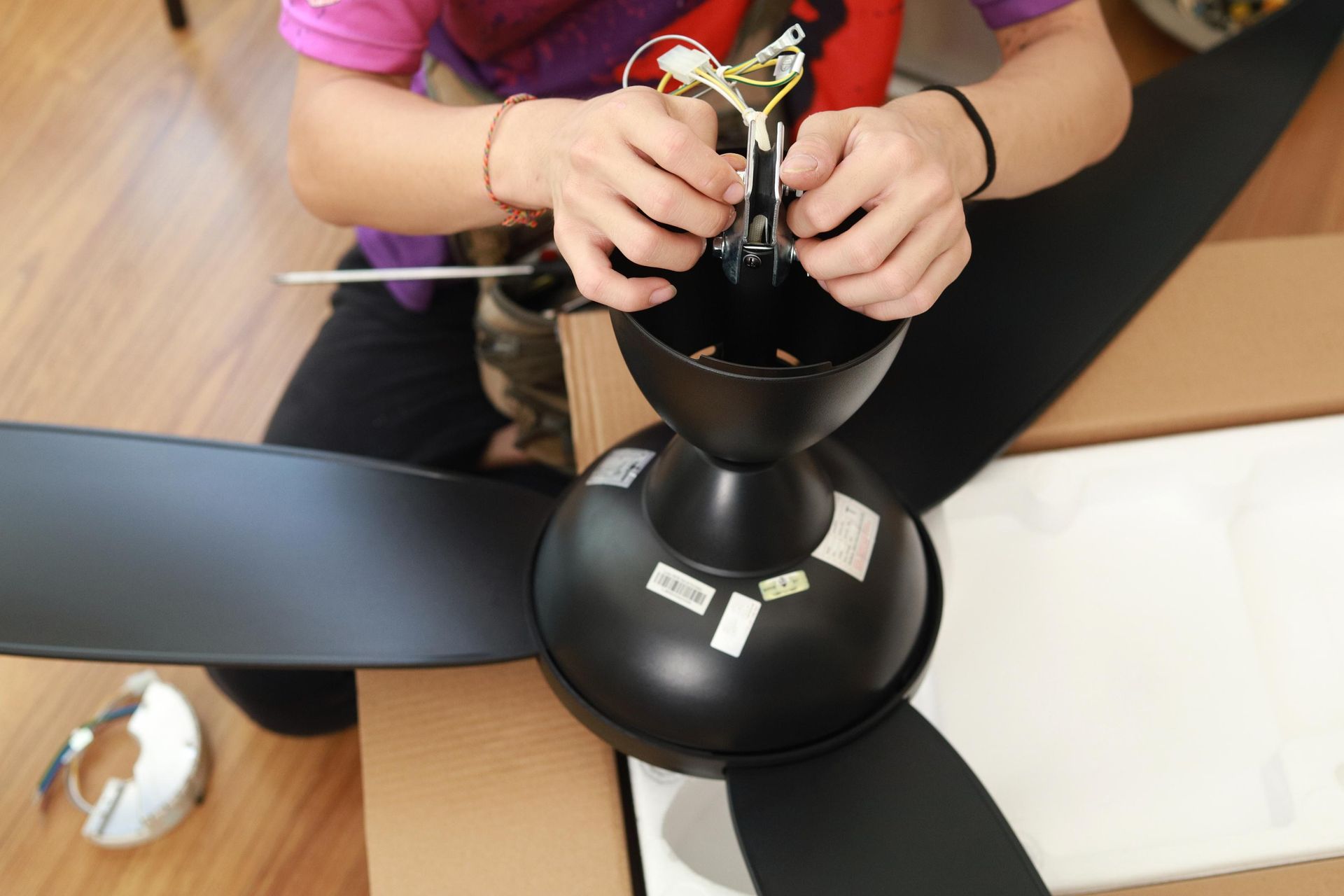 A person is working on a black ceiling fan.