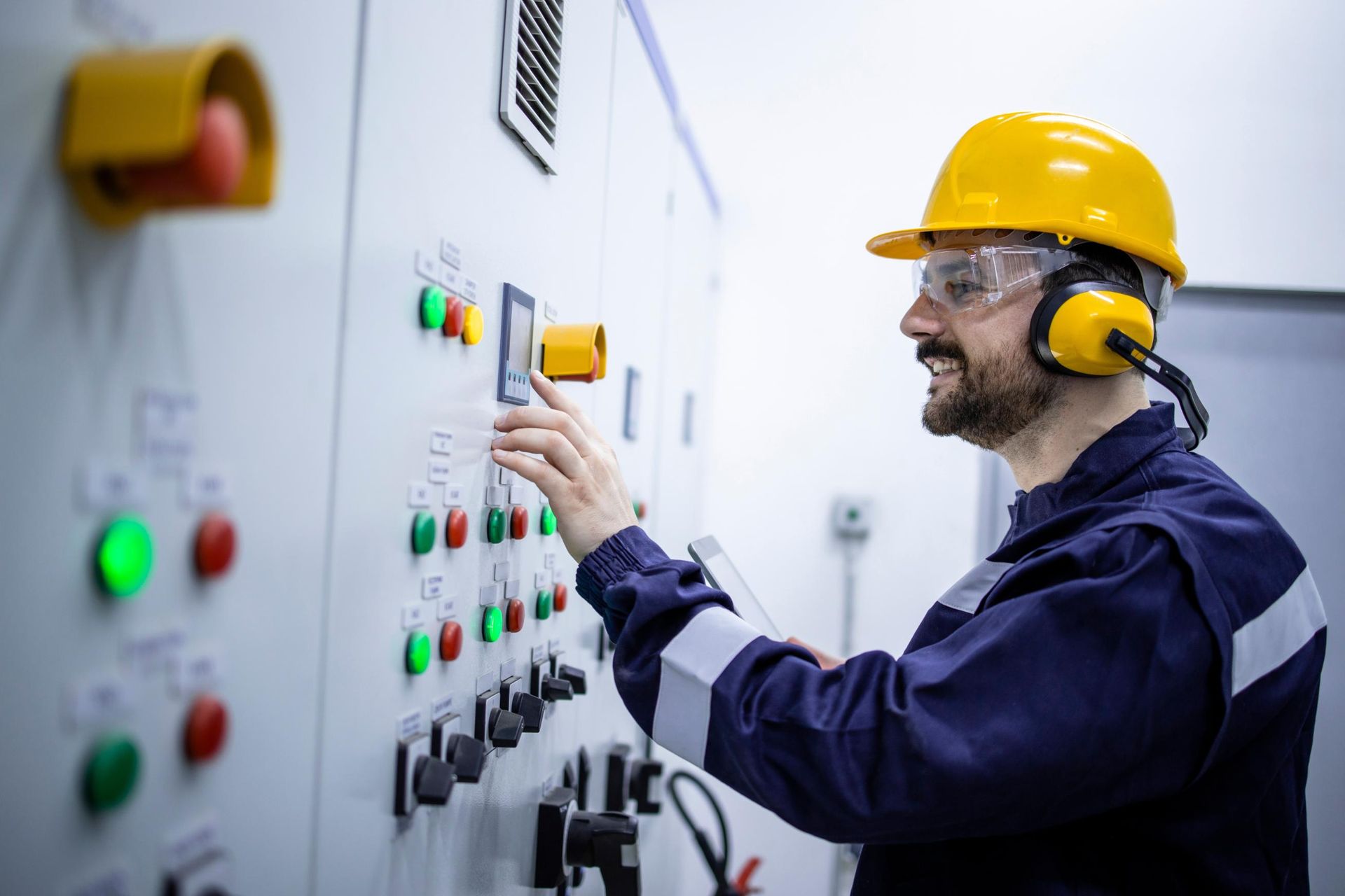 A man wearing a hard hat and ear muffs is working on a control panel.