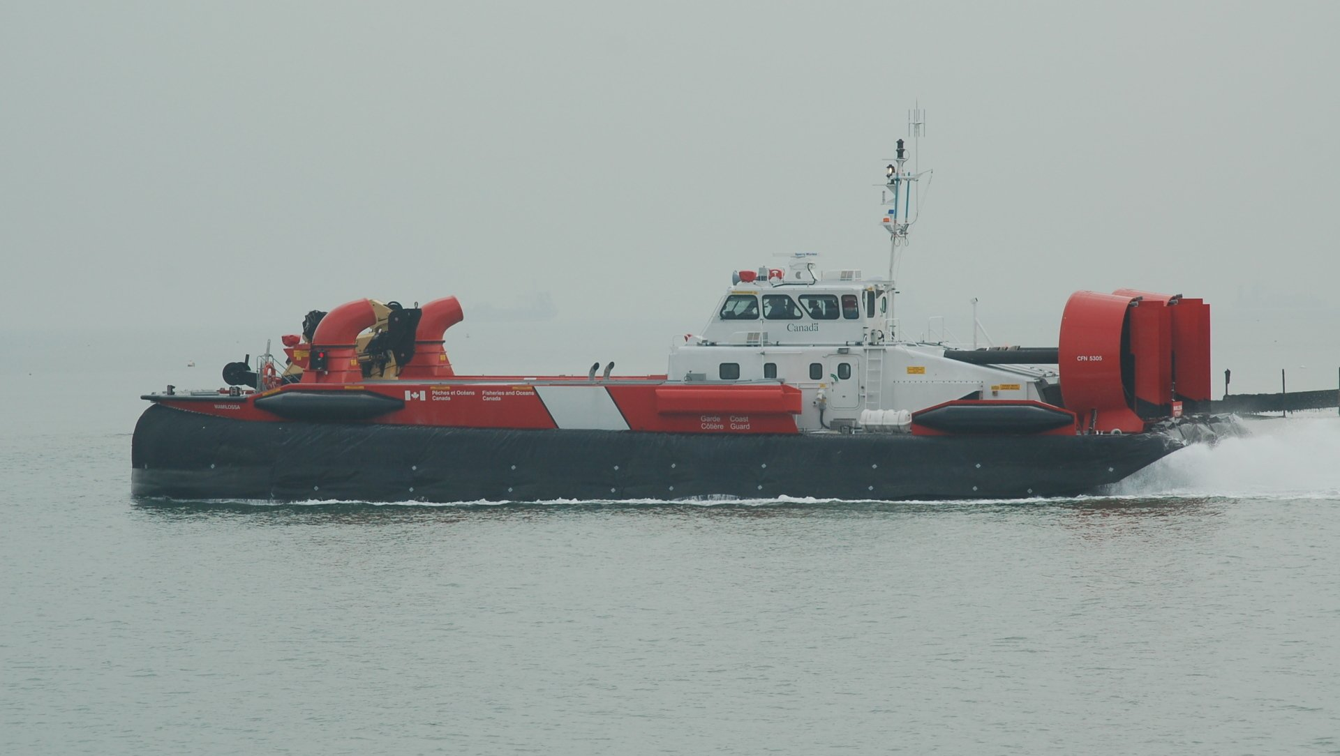 Red-and-white tugboat on calm gray water in a misty harbor.