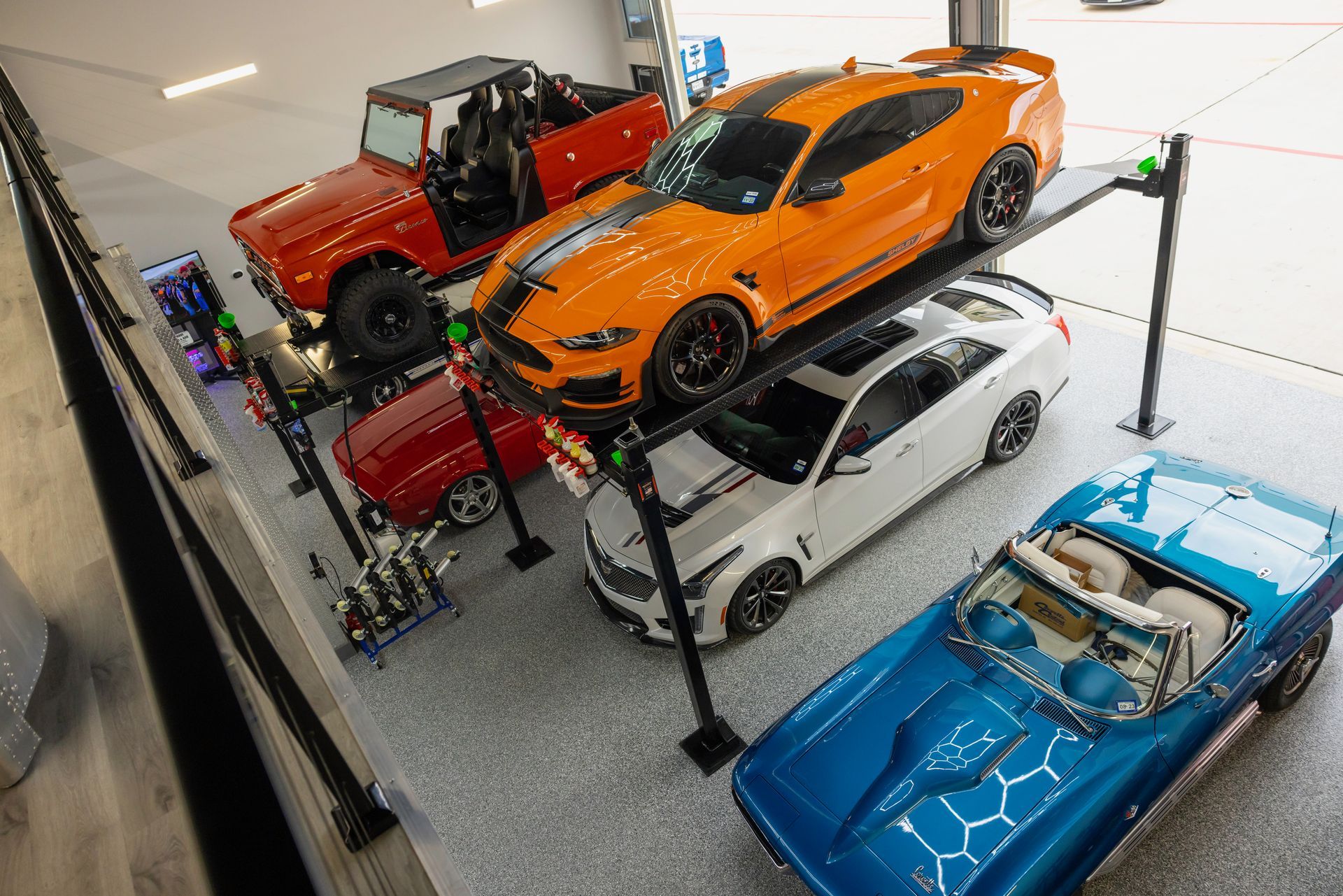 Garage with orange Mustang on a car lift, red Bronco, other cars, and blue convertible. | Auto Motive