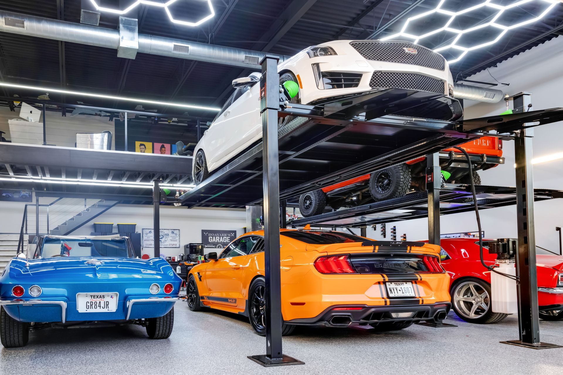 A multi-level garage with stacked sports cars. A blue Corvette, orange Mustang, and others are present. | Auto Motive
