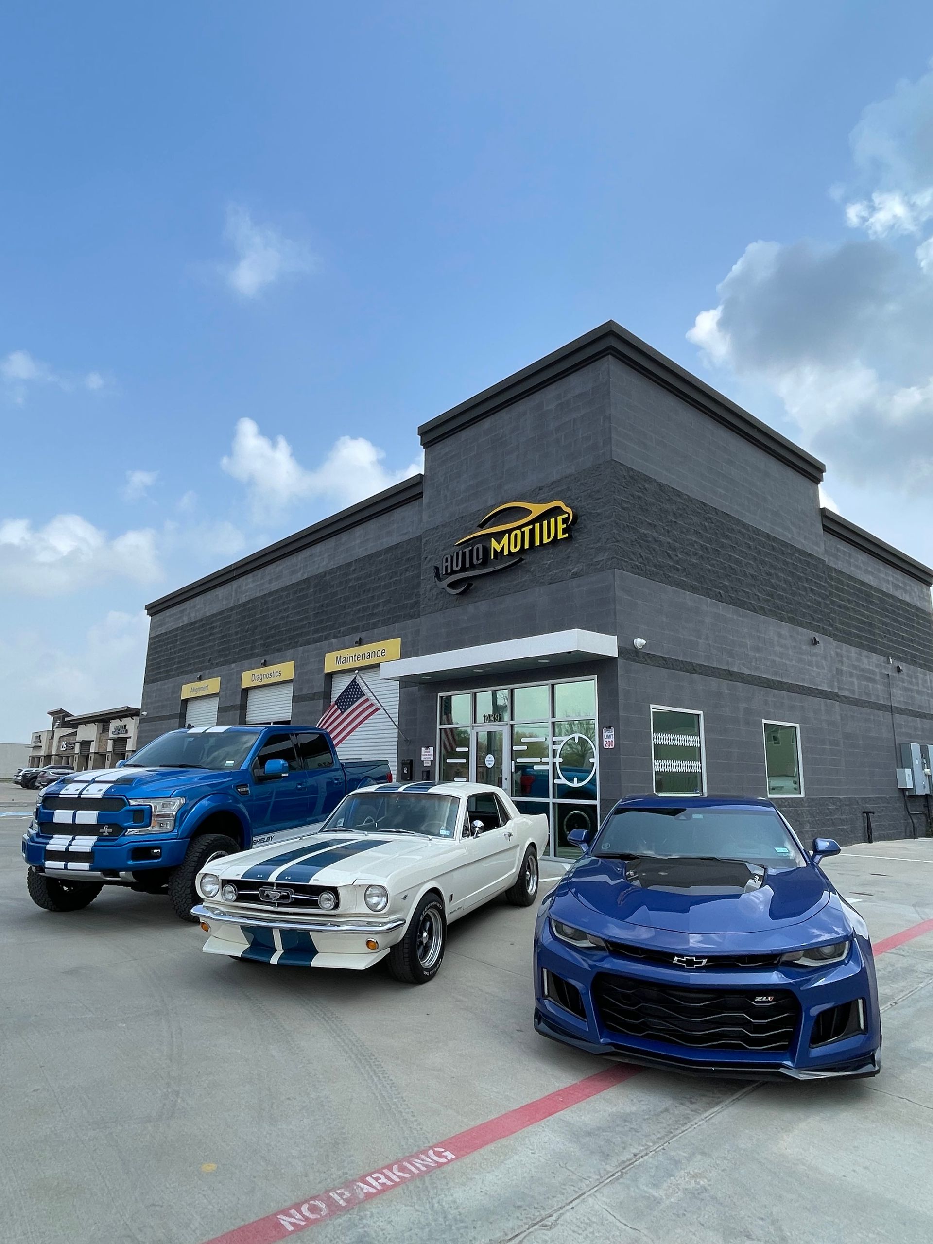 Blue and white cars parked outside a black business building with a blue sky. | Auto Motive